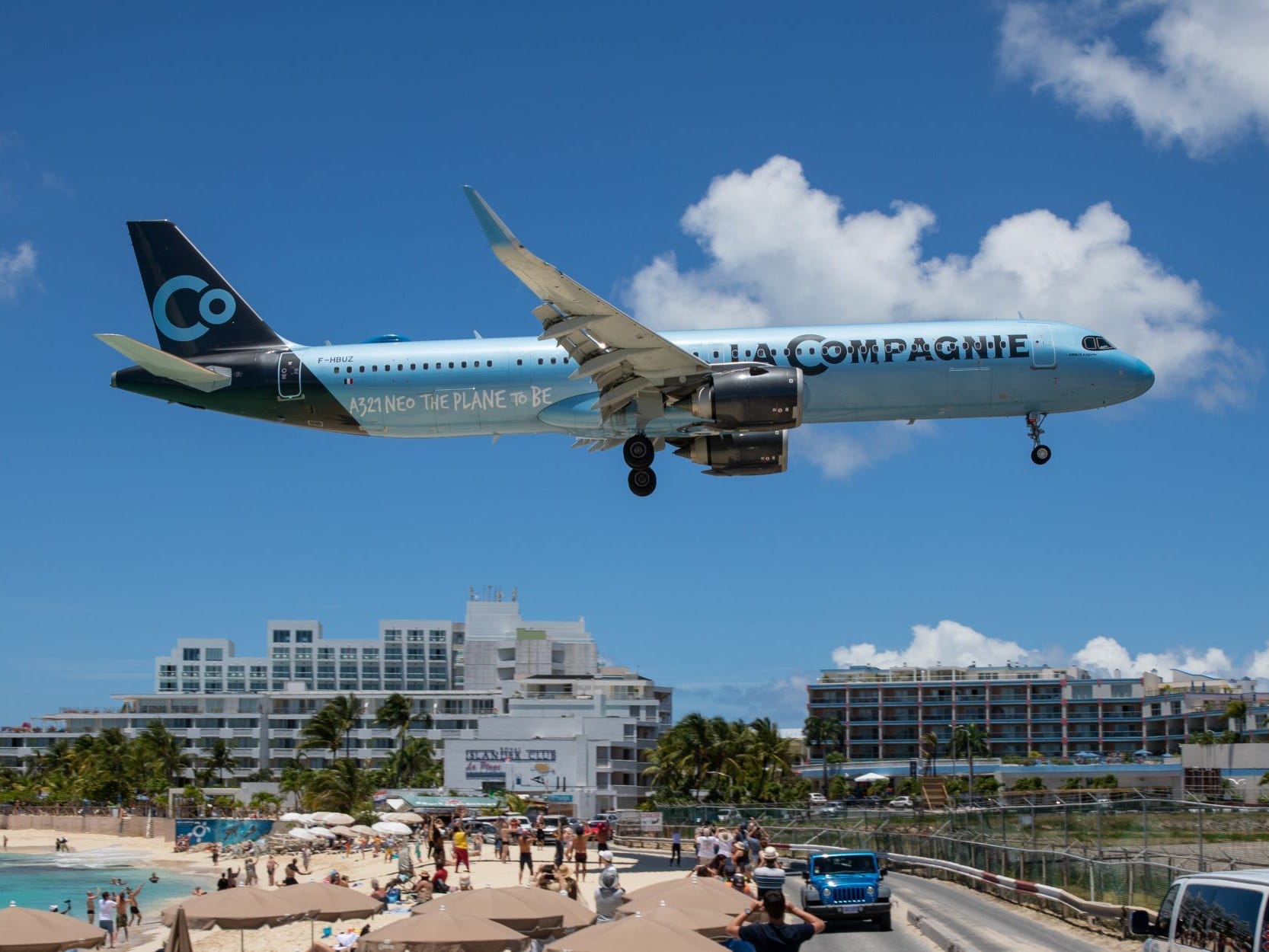 Ein himmelblaues La Compagnie-Flugzeug fliegt über einen Strand in St. Maarten, während es sich auf die Landung vorbereitet.