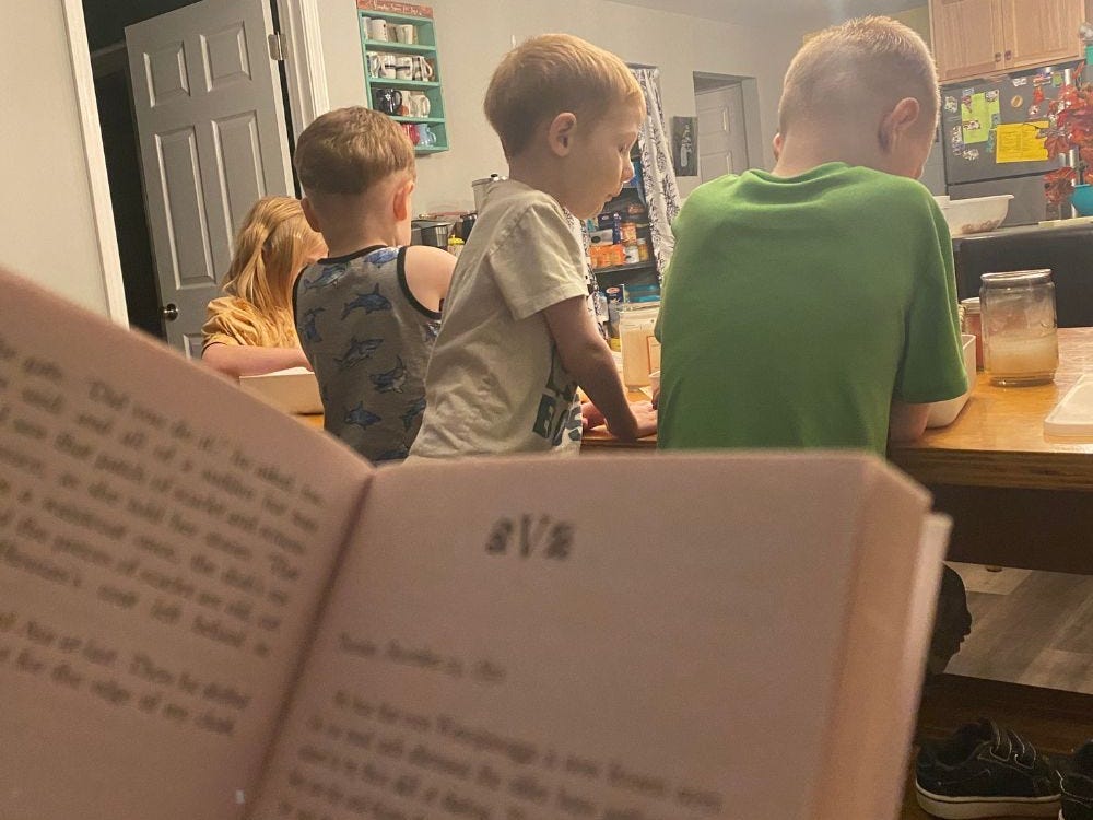 Person hält ein Buch und liest den Kindern am Küchentisch vor