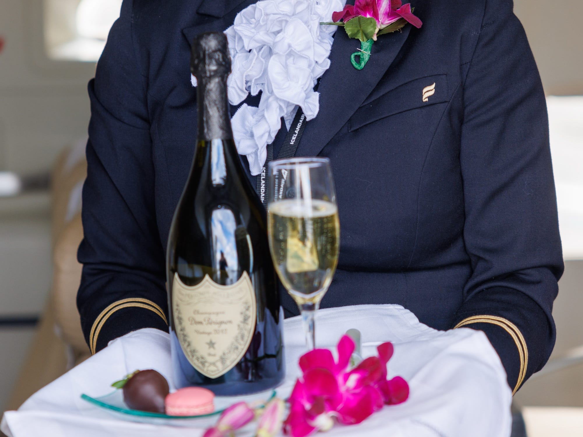 Eine A&K-Flugbegleiterin hält ein Tablett mit Champagner und Blütenblättern als Dekoration in der Hand.