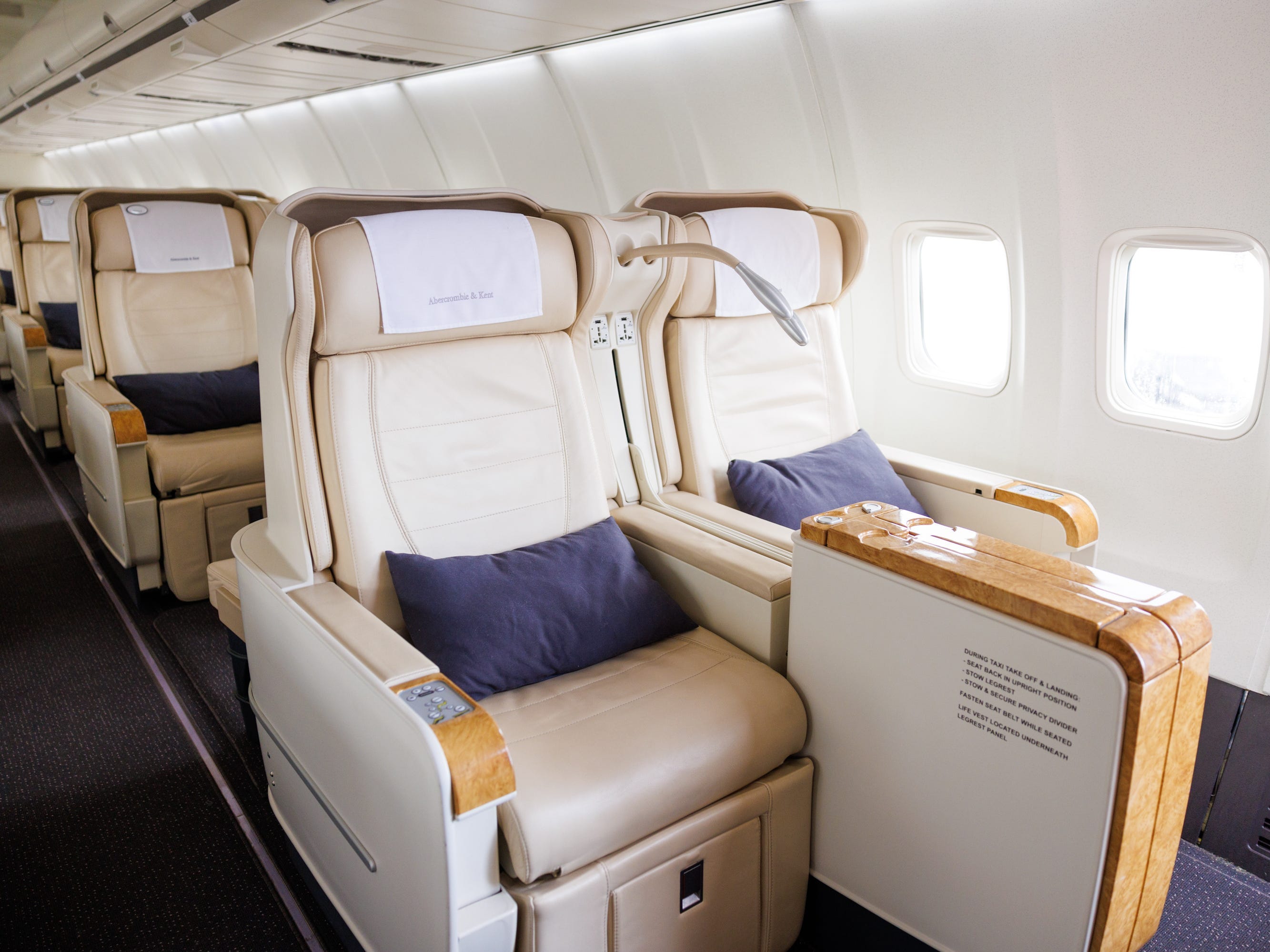 Reihen cremefarbener Sitze an Bord der Boeing 757 der Marke A&K, alle völlig aufrecht mit blauen Kissen auf dem Sitz.