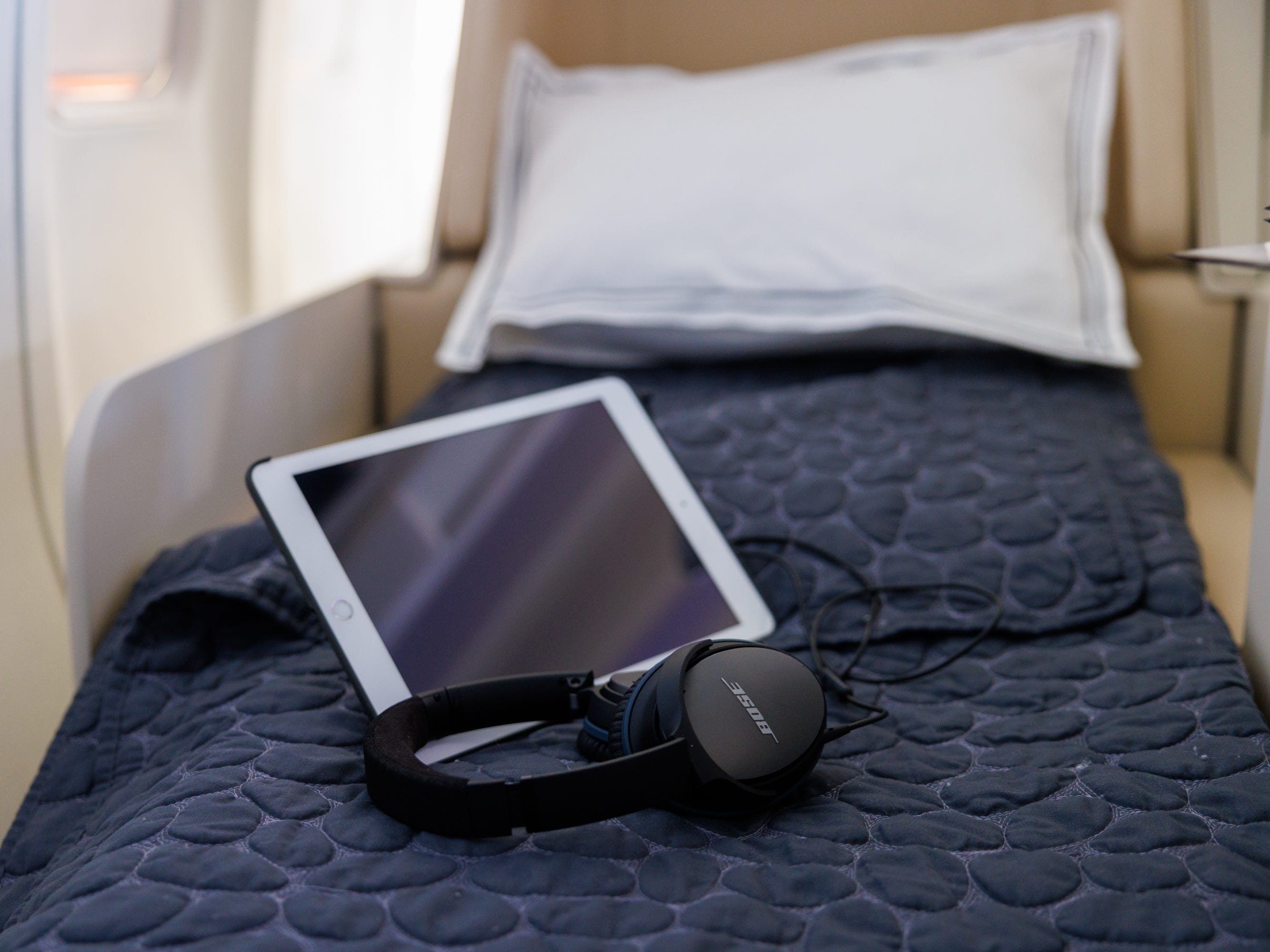 Ein weißes iPad und geräuschunterdrückende Bose-Kopfhörer auf dem Liegebett.