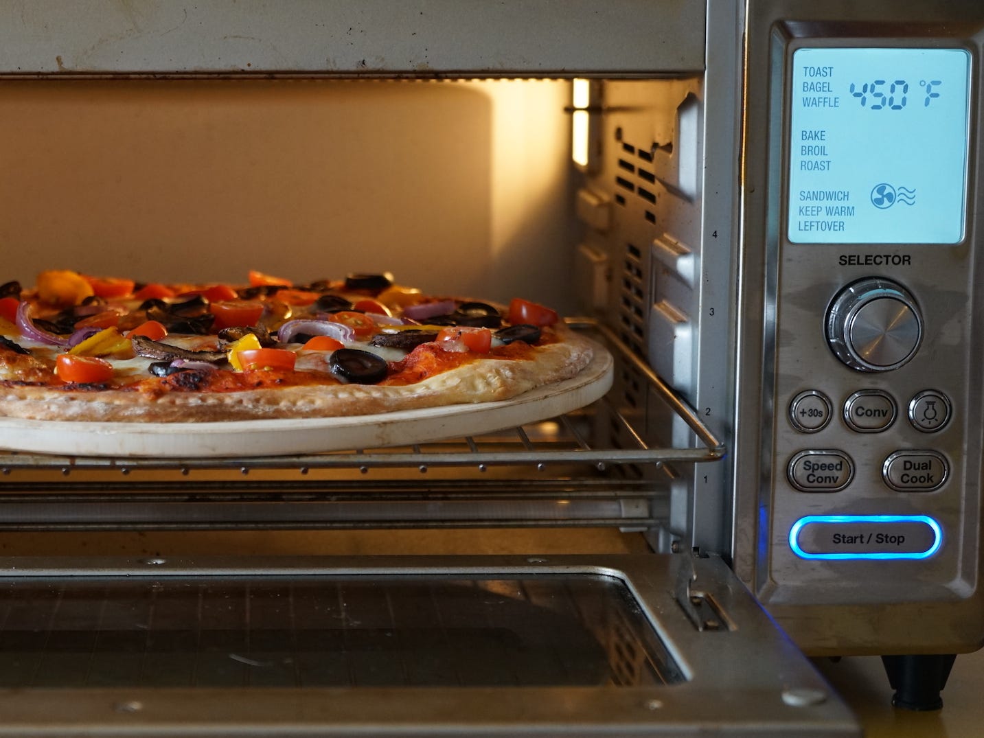 Pizza wird in einen Konvektions-Toasterofen von Cuisinart Chef gelegt, wobei auf dem Bedienfeld 450 Grad Fahrenheit angezeigt werden.