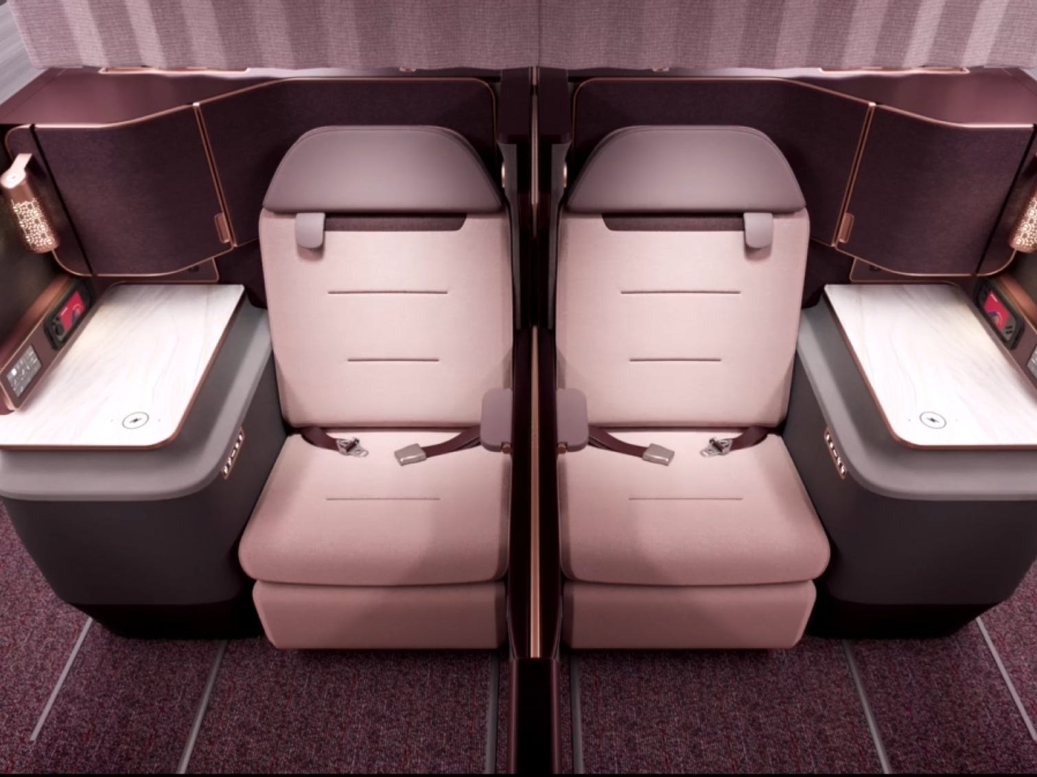 Zwei rosa First-Class-Sitze nebeneinander mit Armlehnen und Lampen auf beiden Seiten.