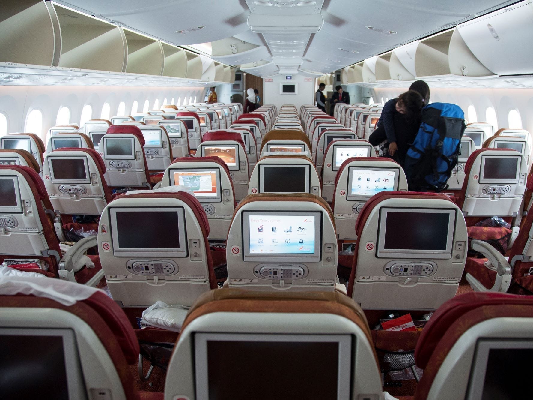 Innenraum der aktuellen 787 mit roten und gelben Sitzen und veralteten Bildschirmen.