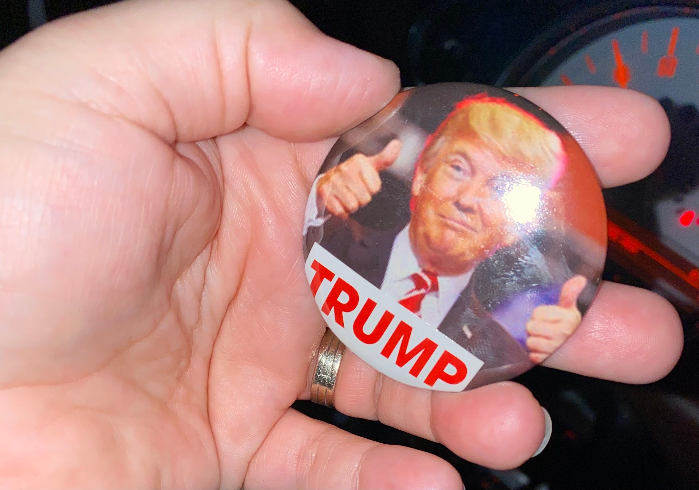 Frau hält einen Knopf in der Hand, auf dem Donald Trump zwei Daumen nach oben zeigt