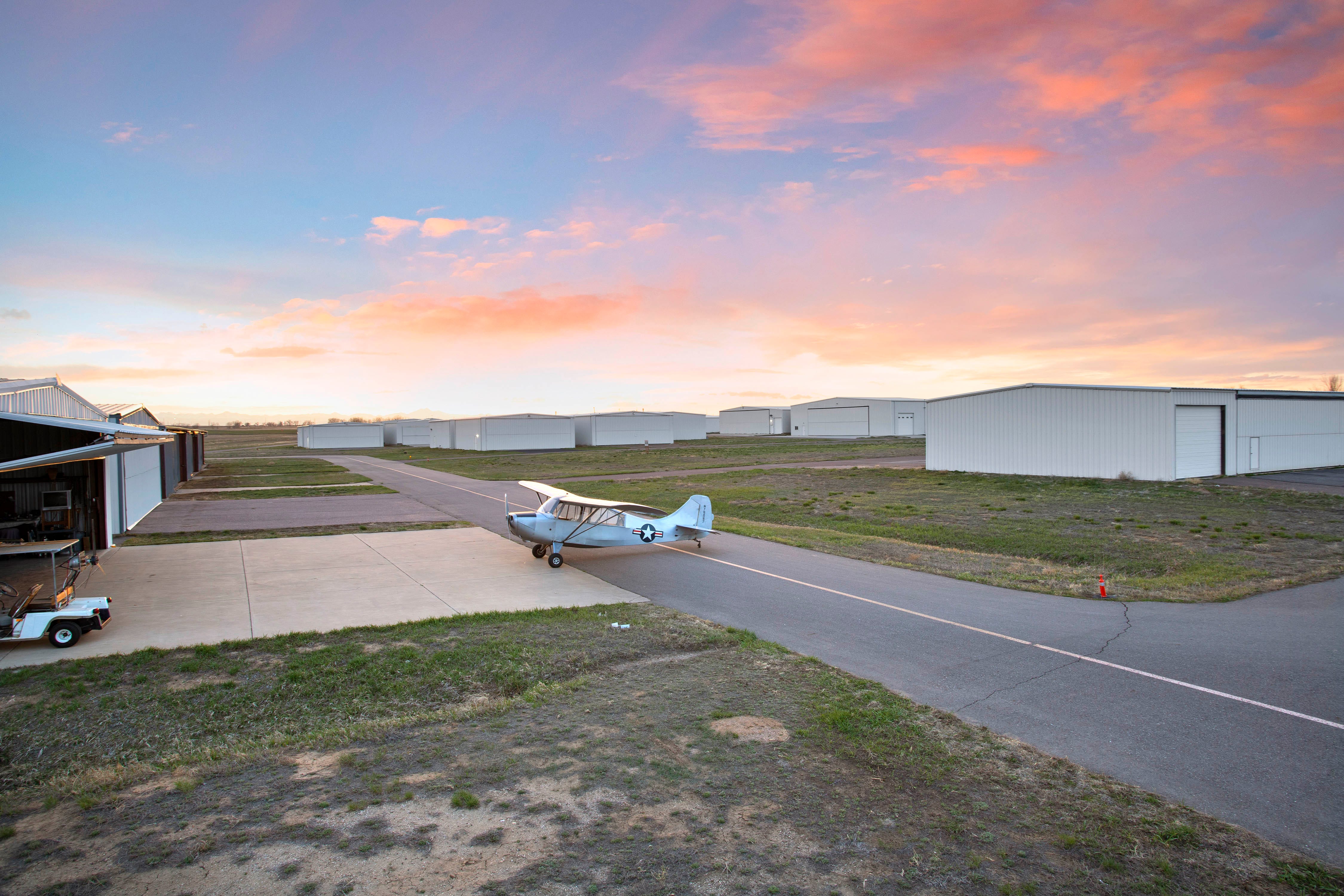 Rosa Wolken am Himmel bei Sonnenuntergang über einem Flugzeug, das auf der Landebahn geparkt ist