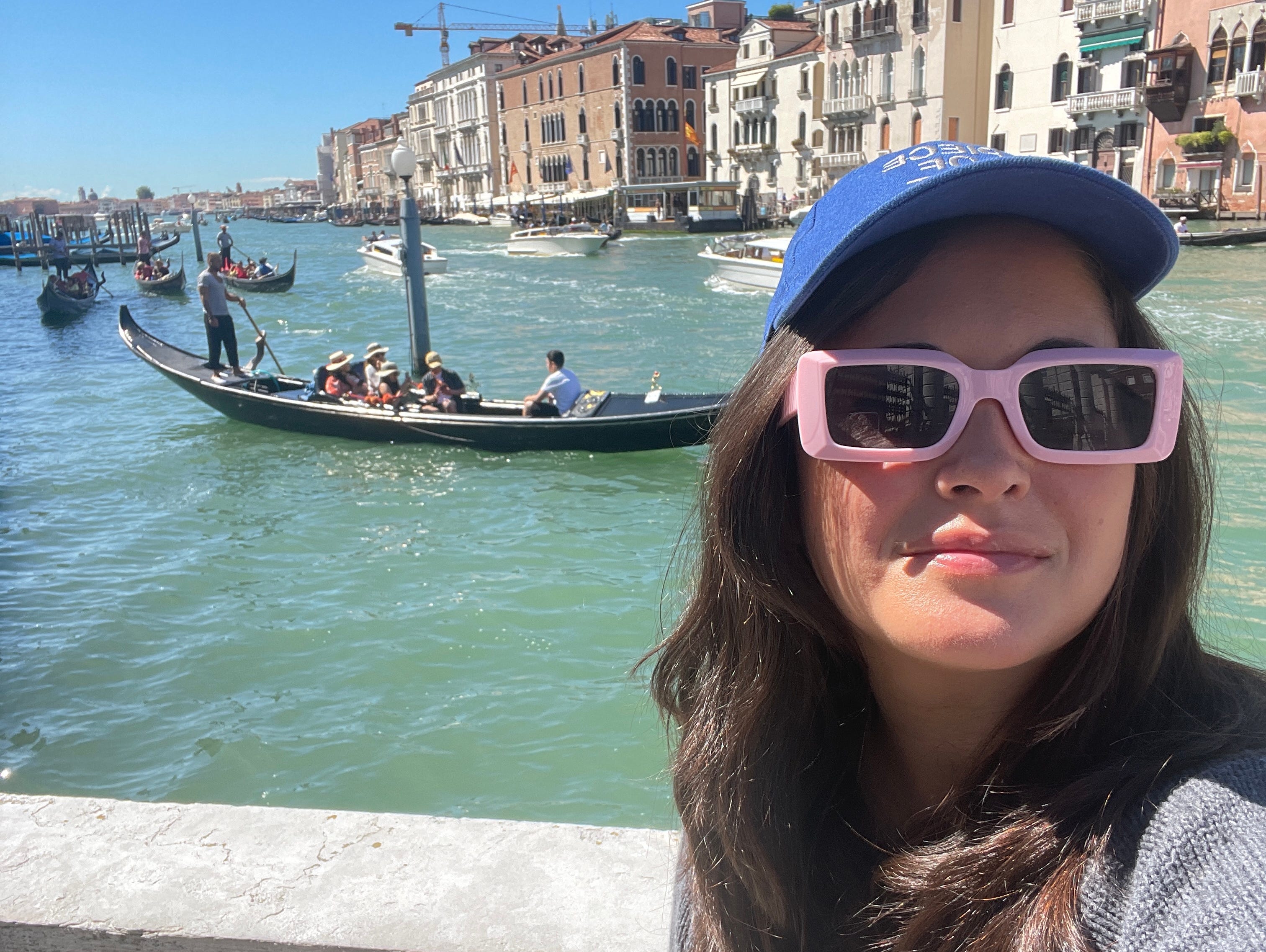 Katka Reversosova mit Hut und Sonnenbrille lächelt in Venedig vor einem Boot voller Menschen