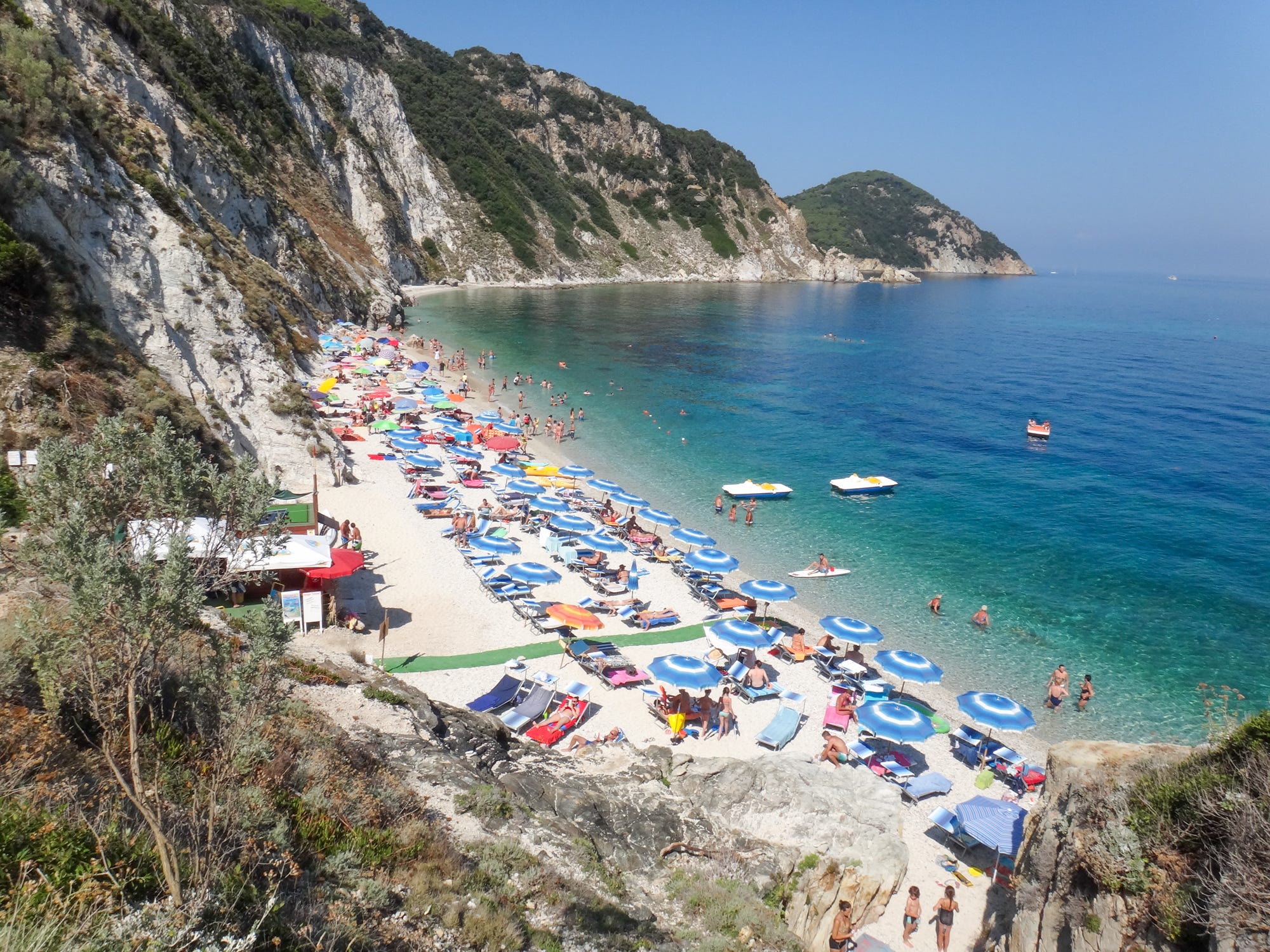 Blick auf die Insel Elba mit Steinen, Sandstränden mit Sonnenschirmen und Handtüchern und klarem, blauen Wasser