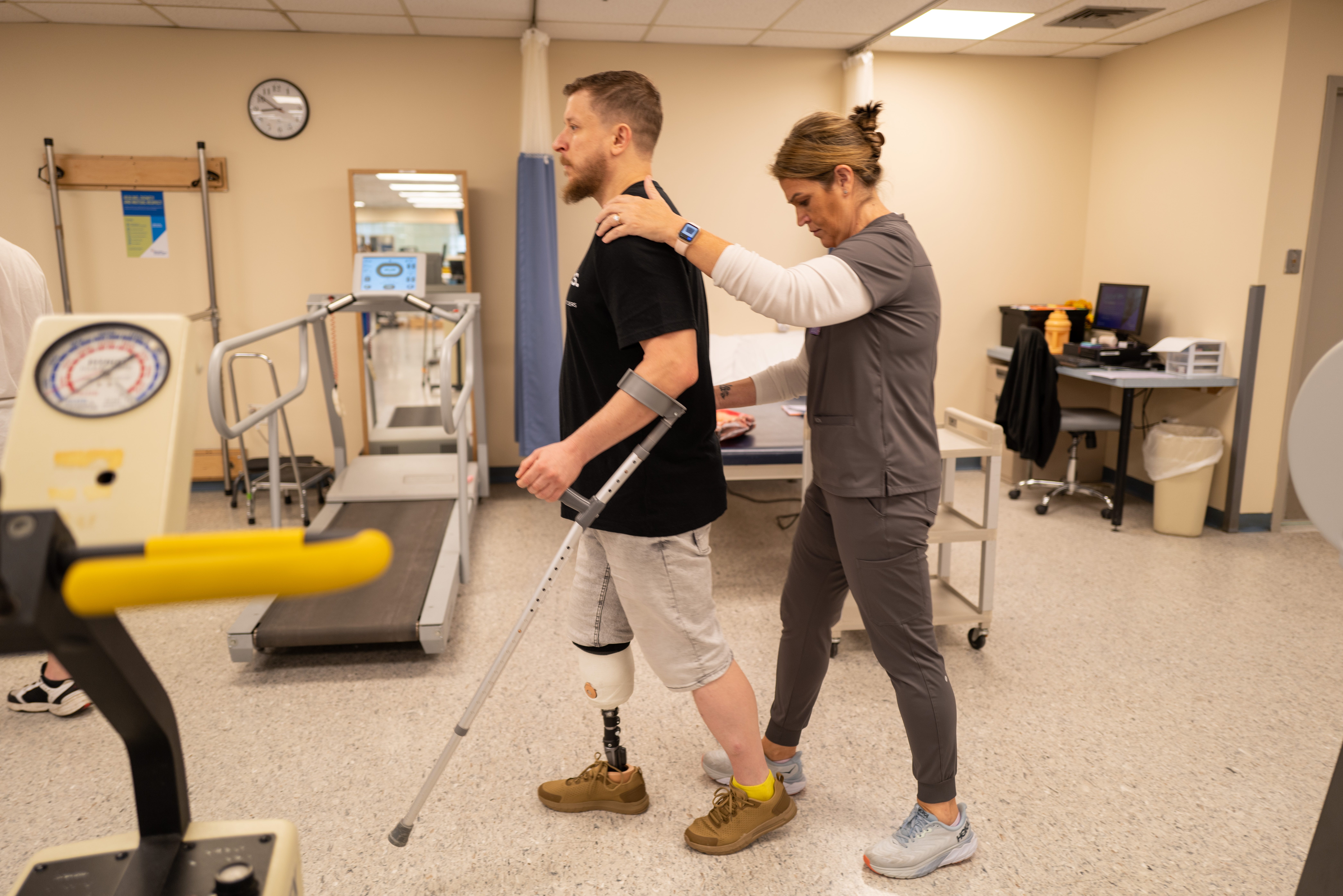 Ein Soldat mit einer Beinprothese wird beim Gehen von einem Physiotherapeuten unterstützt