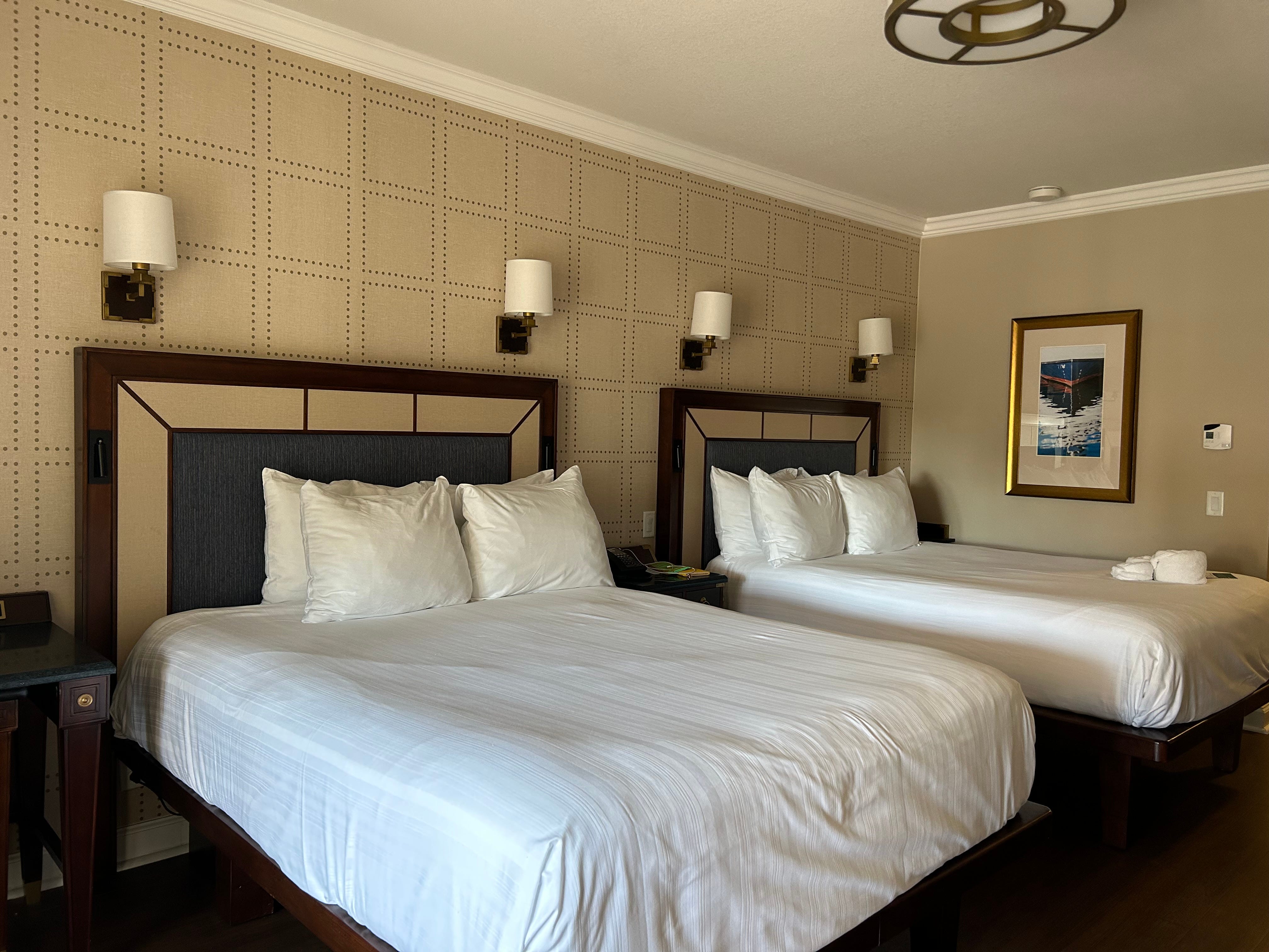 Zwei Betten mit weißen Laken vor einer schlichten beigen Wand in einem Hotelzimmer im Disney Yacht Club