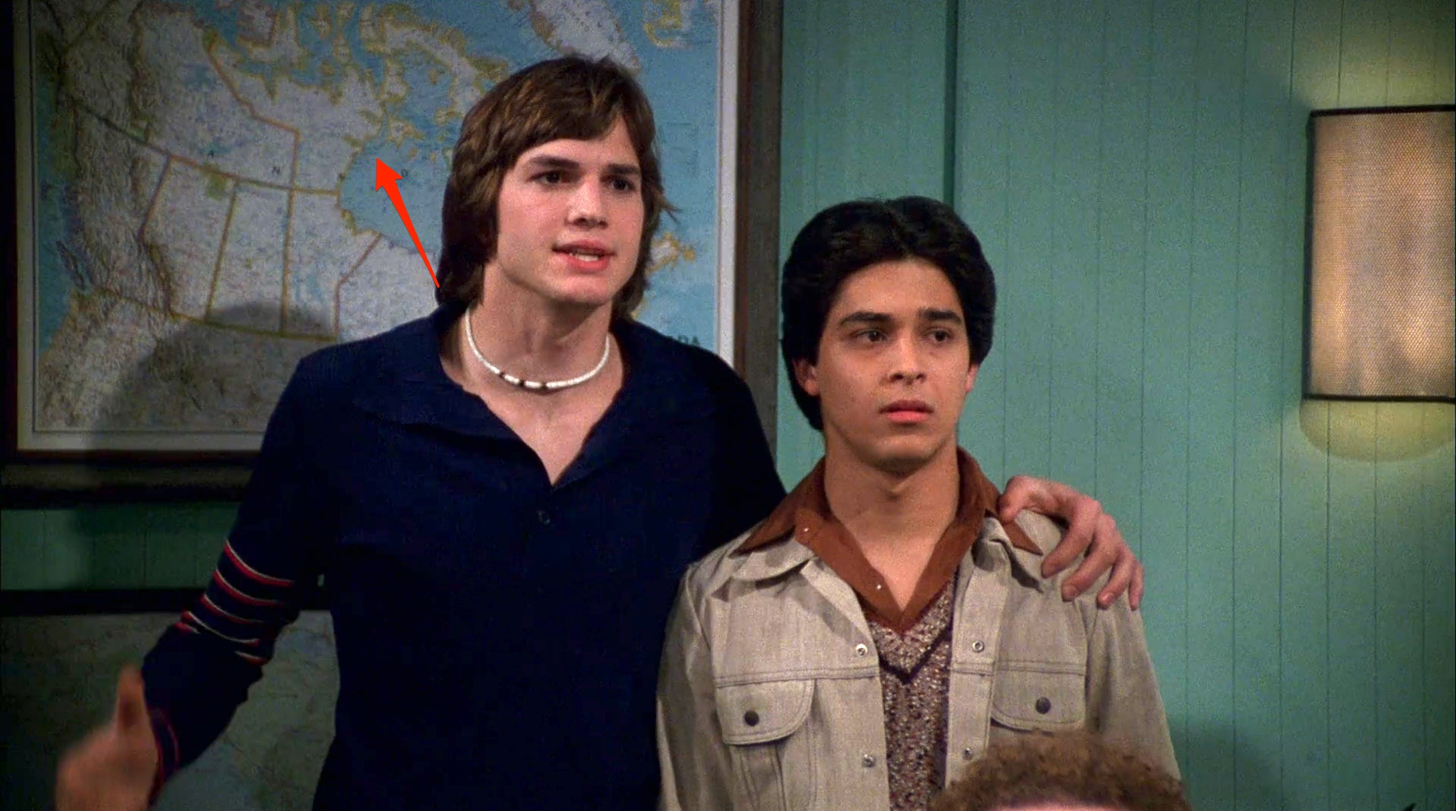 Ein roter Pfeil, der auf eine Karte von Kanada hinter Kelso und Fez in der dritten Staffel von „That '70s Show“ zeigt.