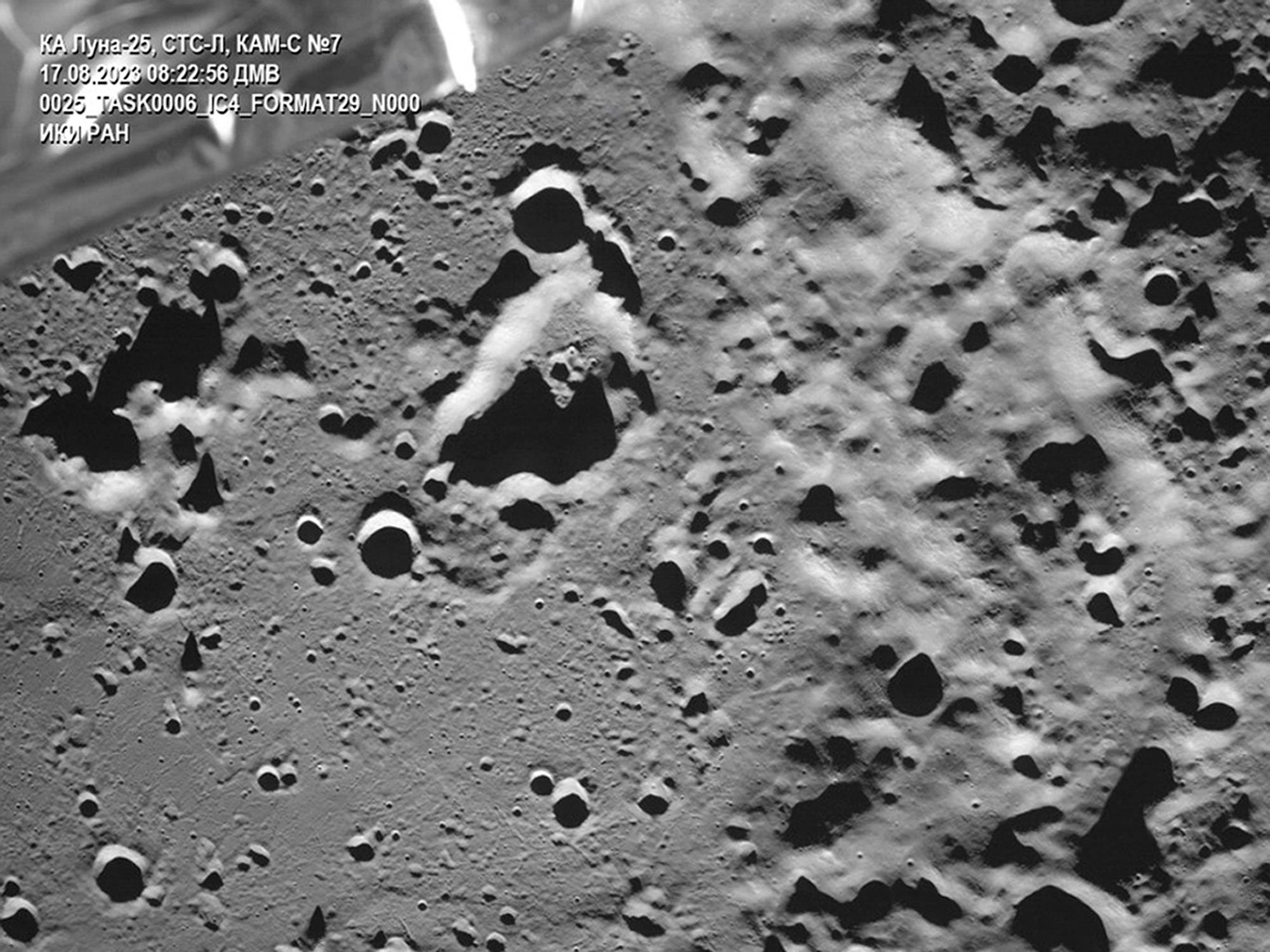 Die Oberfläche eines mondgrauen Felskraters ist mit einem Teil der Raumsonde Luna 25 in der oberen linken Ecke sichtbar