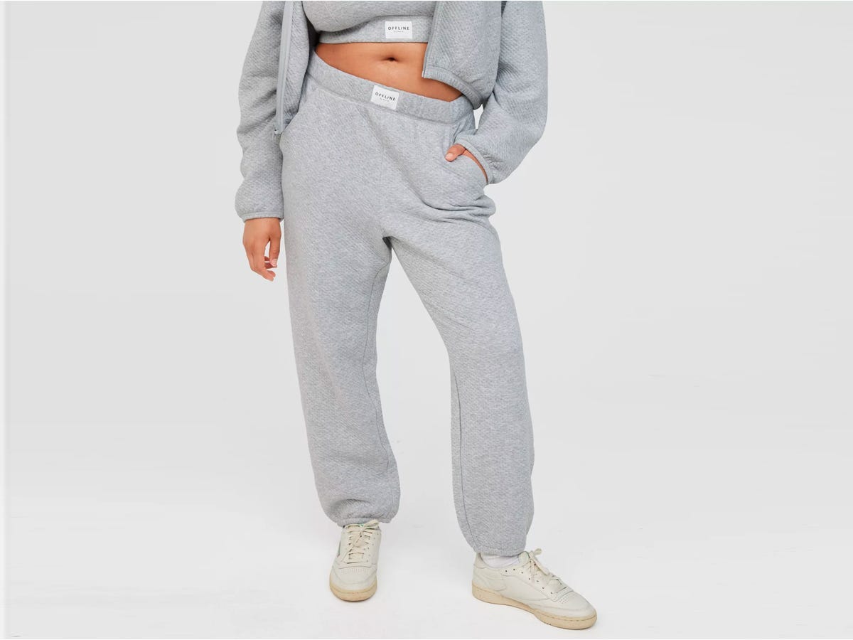 Das abgebildete Modell trägt von der Taille abwärts graue OFFLINE By Aerie Coffee Run Joggers mit einem passenden Sweatshirt und Turnschuhen.