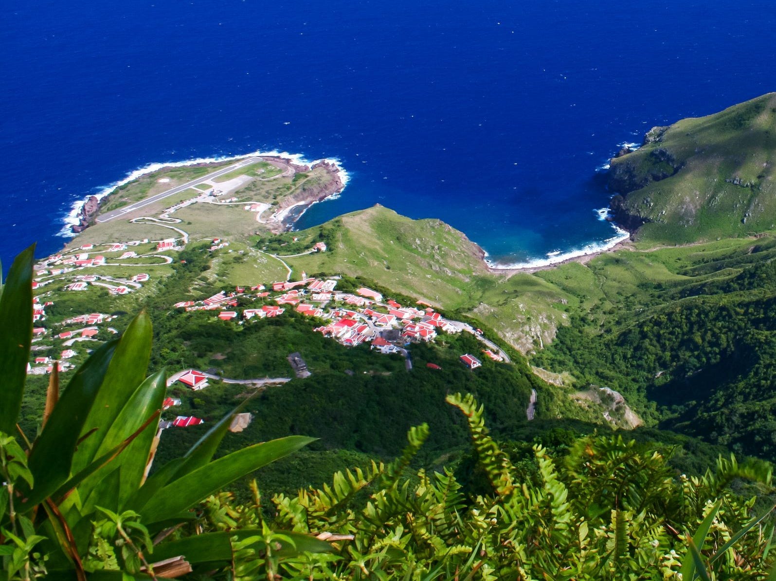 Eine Draufsicht auf die Insel Saba mit dem Flughafen oben links im Bild und dem blauen Meer im Hintergrund.
