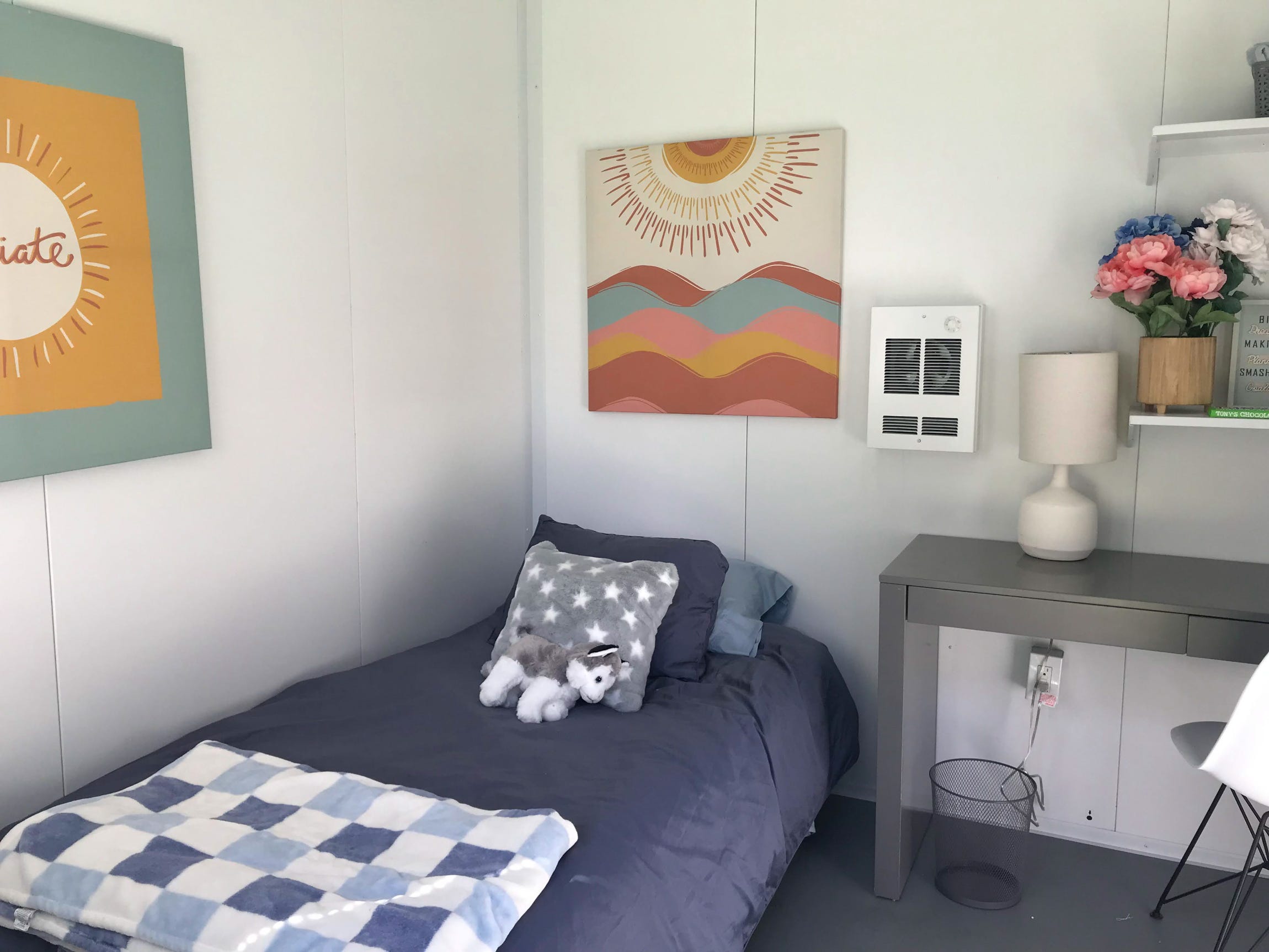 Ein Bett, eine Wanddekoration und ein Nachttisch in einem Tiny House am Standort Santa Barbara von DignityMoves