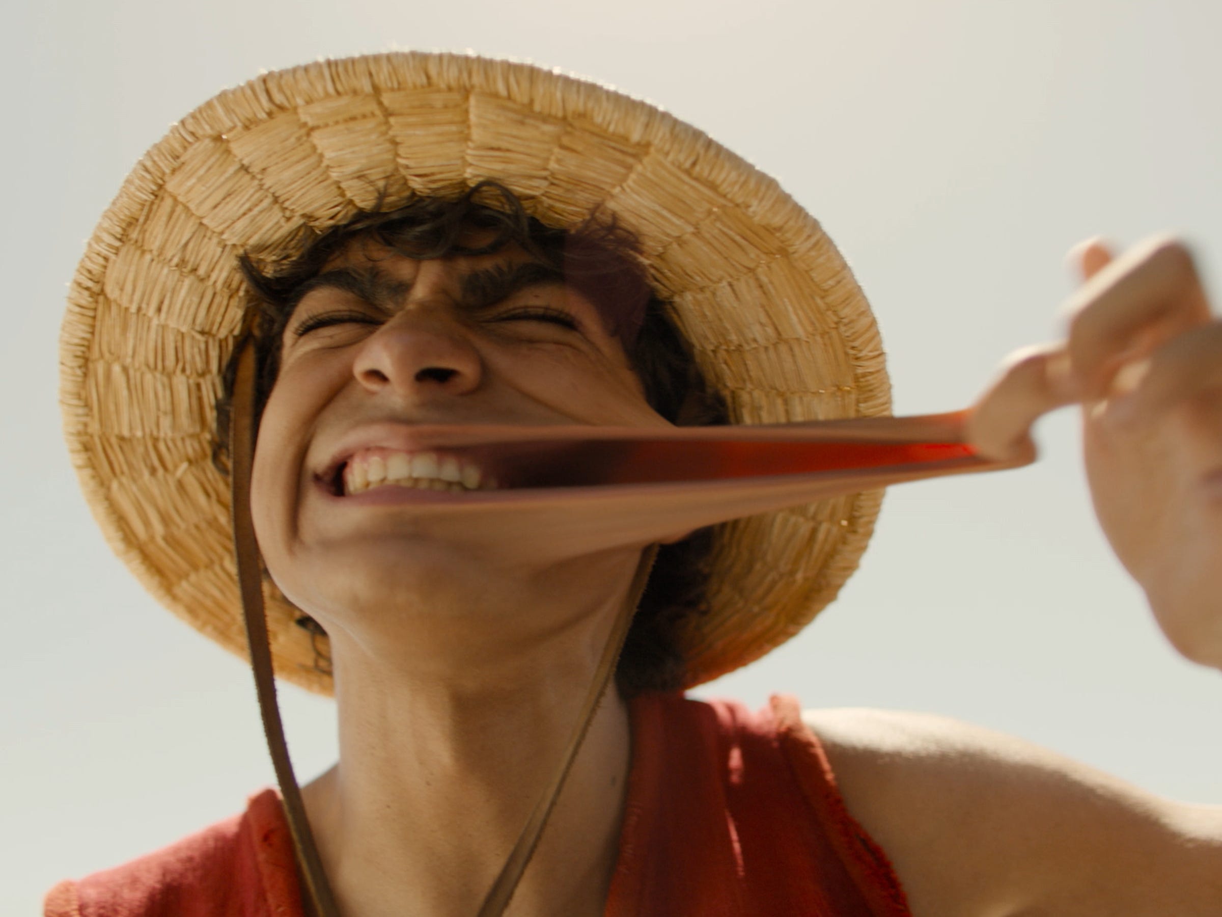 Iñaki Godoy als Ruffy in Netflixs One Piece.  Er streckt seine Wange heraus, demonstriert, dass er sich wie Gummi dehnen kann, und grinst breit