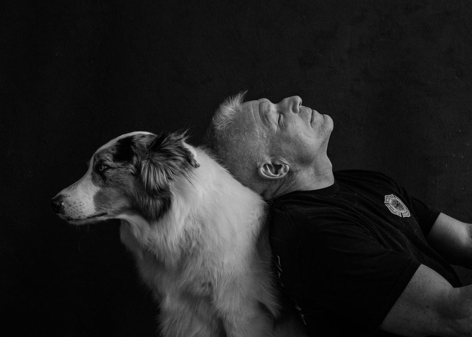 Ein Mann lehnt seinen Kopf zurück auf den Rücken eines Hundes.  Das Bild ist in Schwarzweiß.