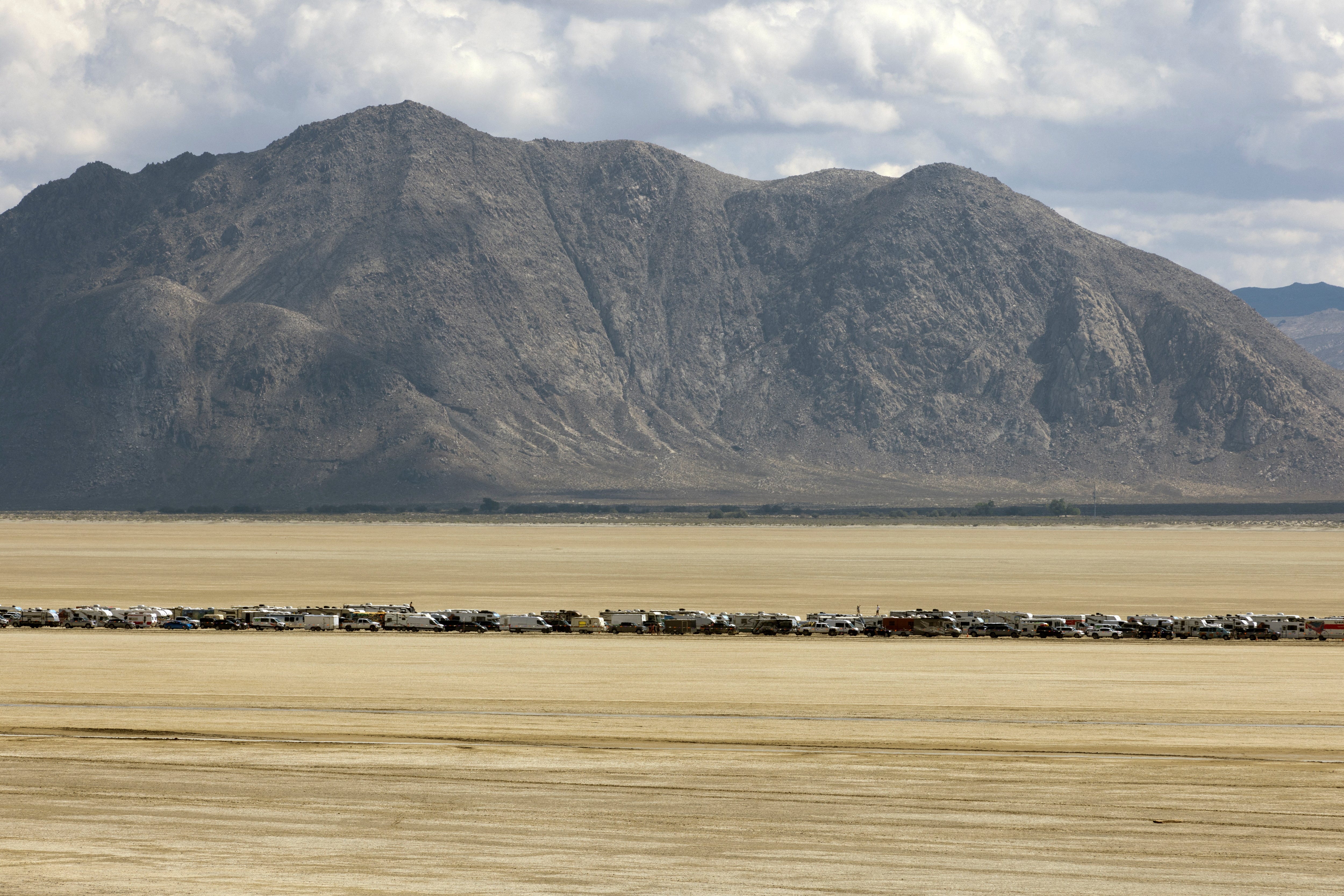 Fahrzeuge verlassen Burning Man vor der Kulisse der Berge Nevadas.