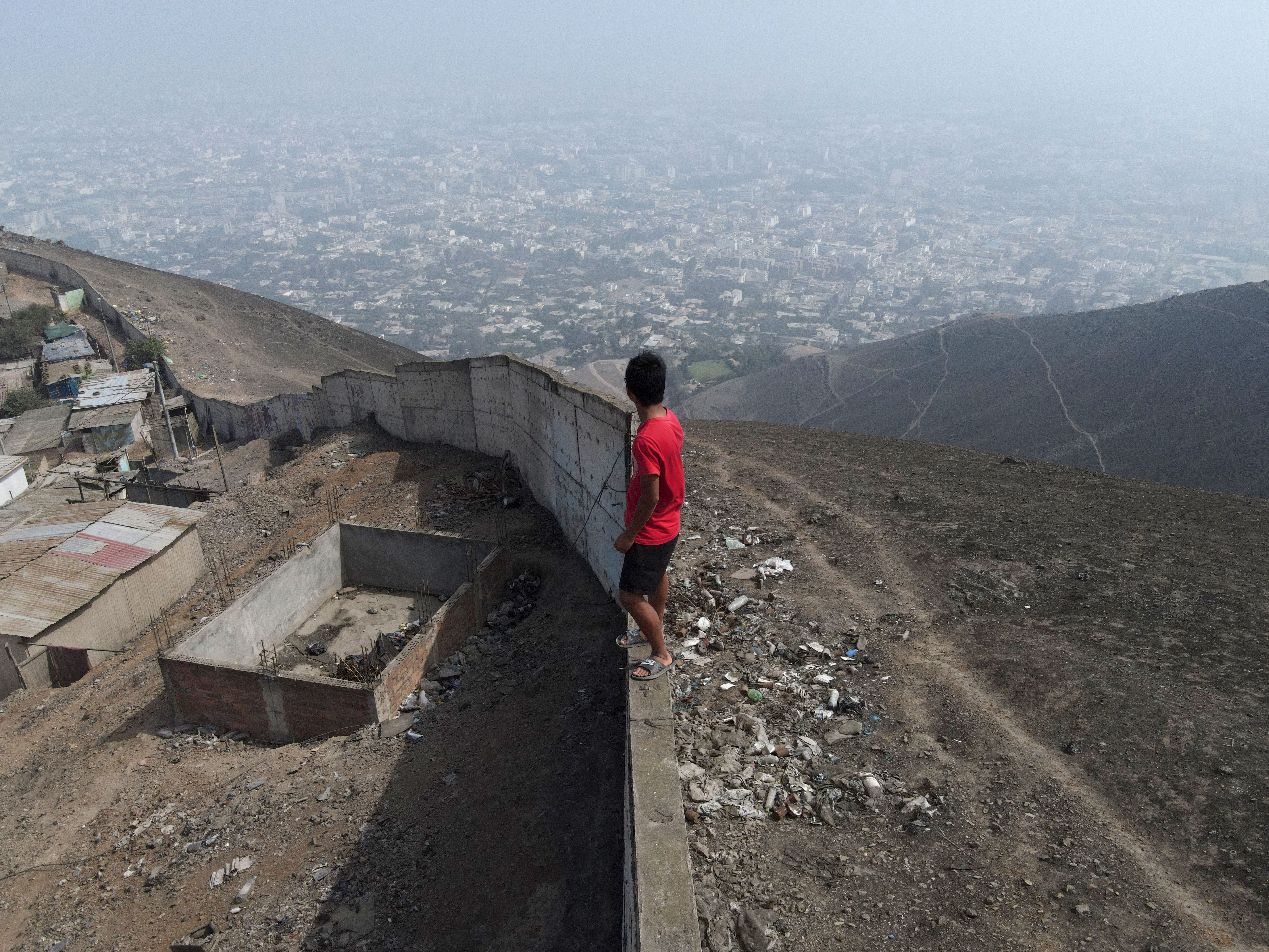 Eine Luftaufnahme eines Jungen, der auf der „Mauer der Schande“ steht, die die exklusivsten und wohlhabendsten Gebiete im Bezirk Santiago de Surco von einer wirtschaftlich benachteiligten Zone im Bezirk San Juan de Miraflores in Lima, Peru, trennt.