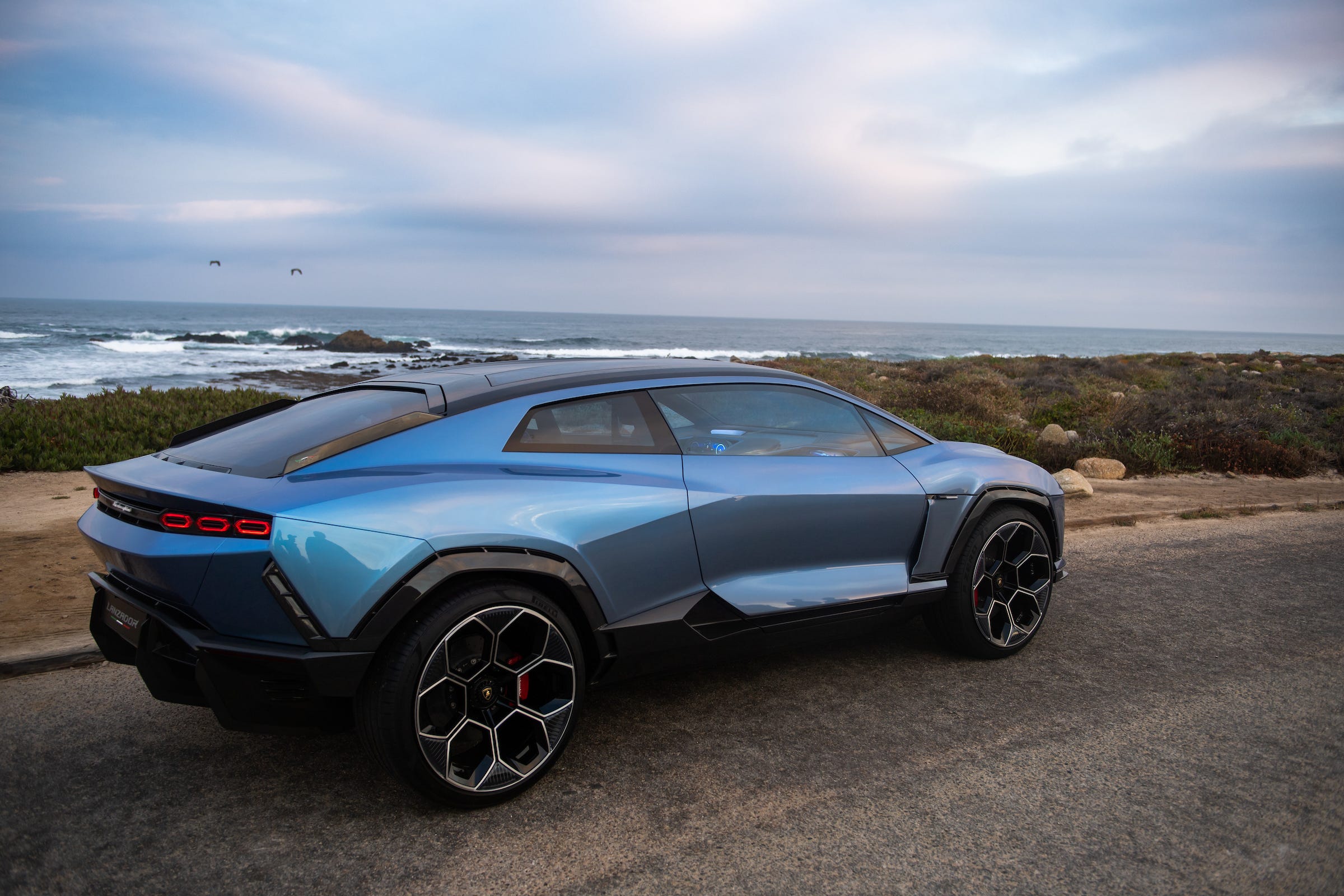 Das Konzeptauto Lamborghini Lanzador vor einem felsigen Strand und einem blauen bewölkten Himmel.