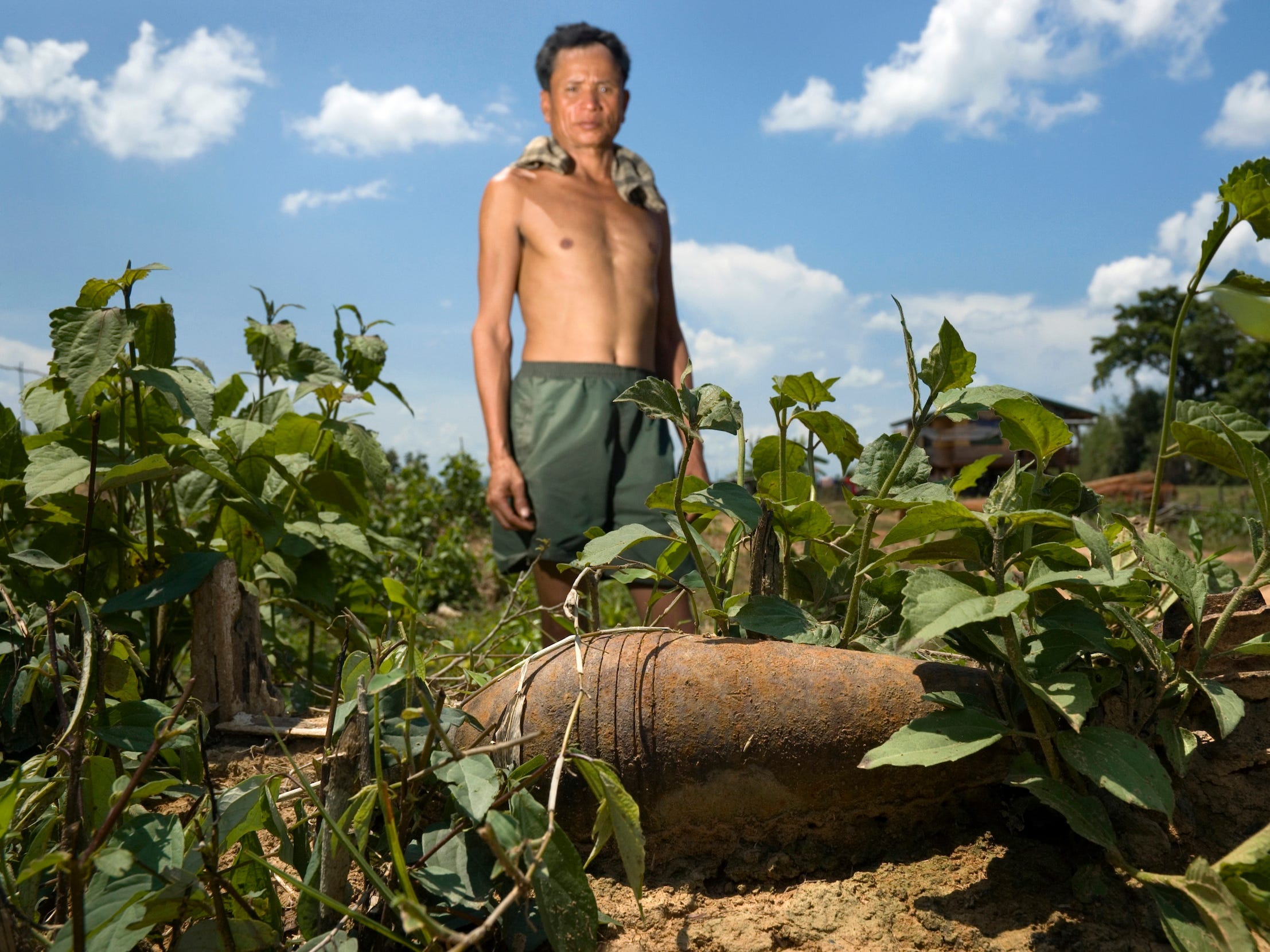 Ein Bauer steht neben einem lebenden Mörser, den er auf seinem Land in Laos gefunden hat.