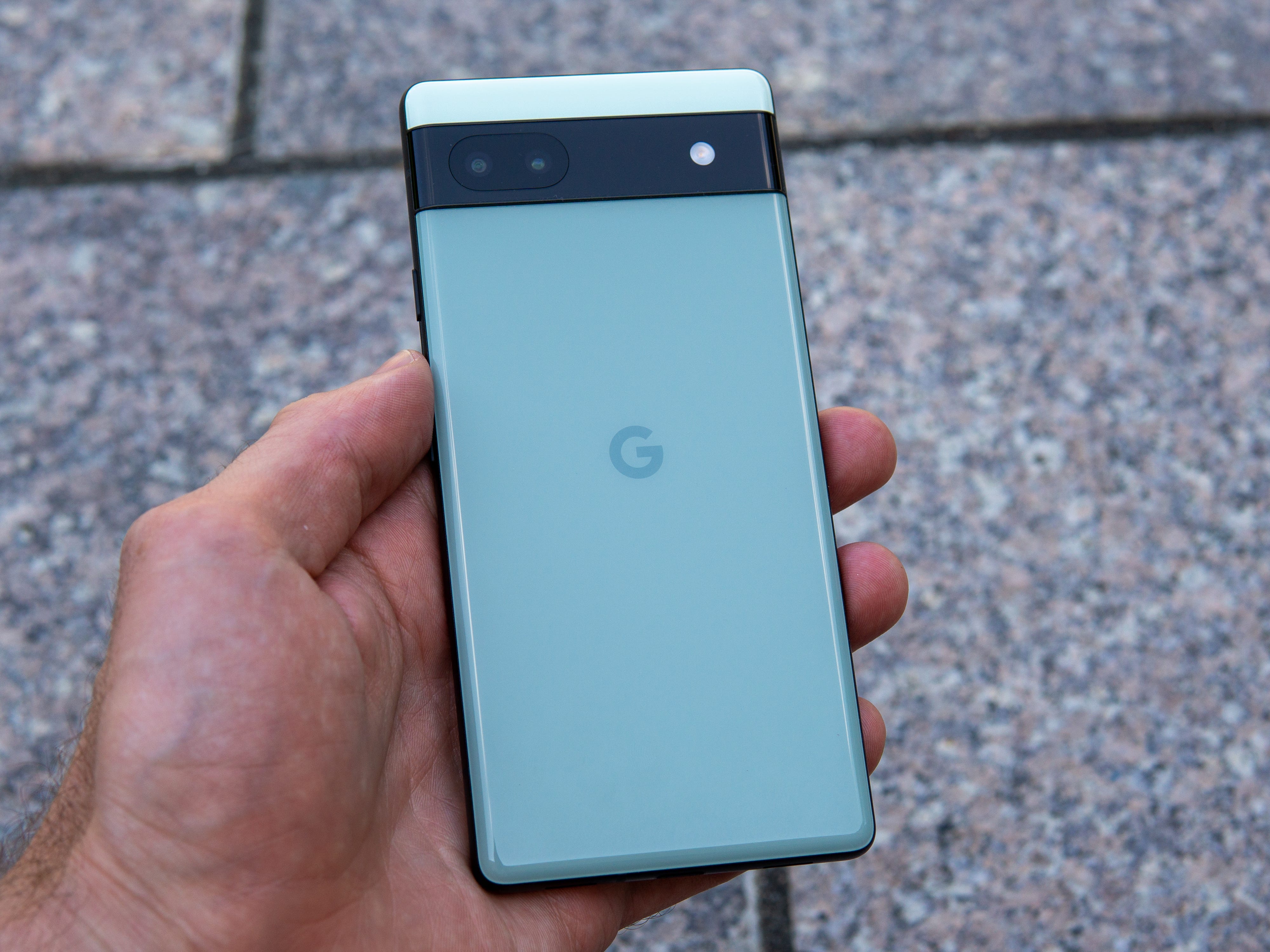 Die Hand einer Person, die das Google Pixel 6a hält, zeigt die Rückseite in der Farboption Salbei.