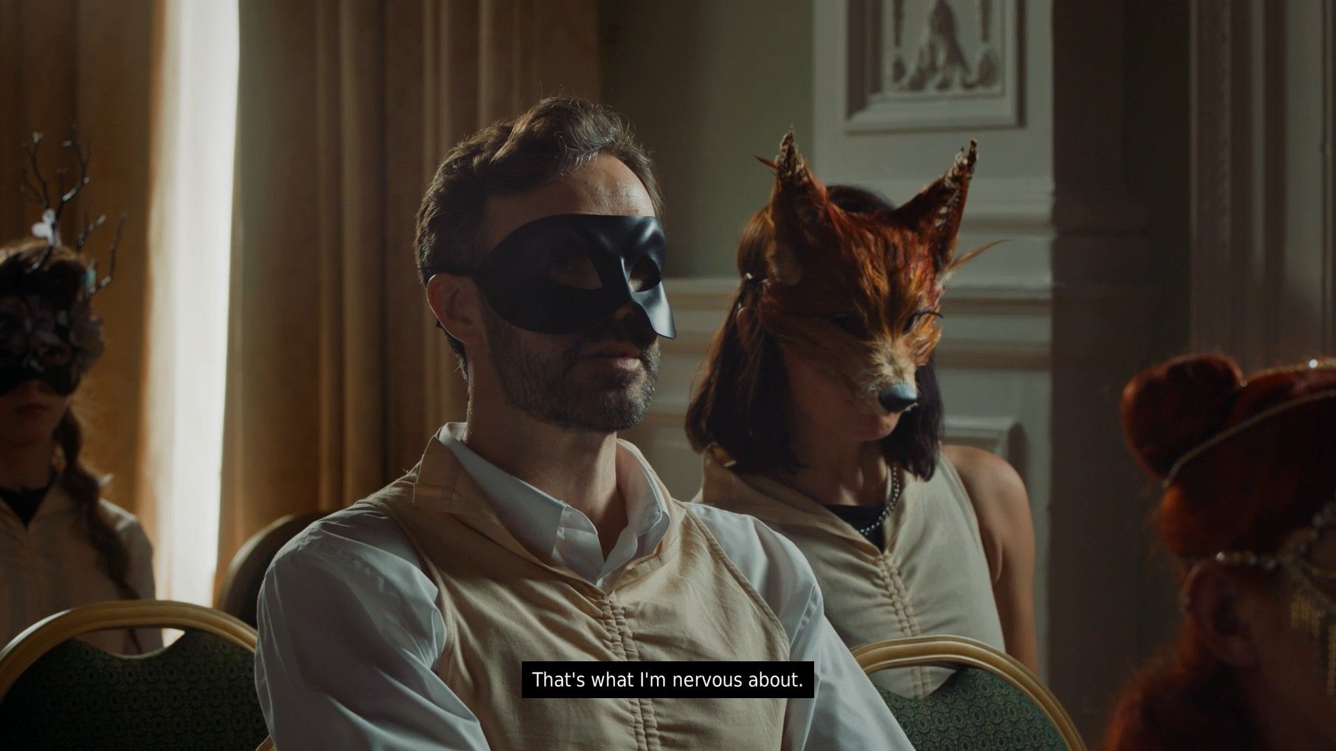 Szene im Isle Tide Hotel, die eine Frau mit einer Fuchsmaske zeigt, die mit Josh in einer schwarzen Maske spricht.