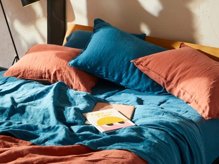 Brooklinen-Leinenbettwäsche in Blau und Terrakotta auf einem Bett mit Büchern darauf.