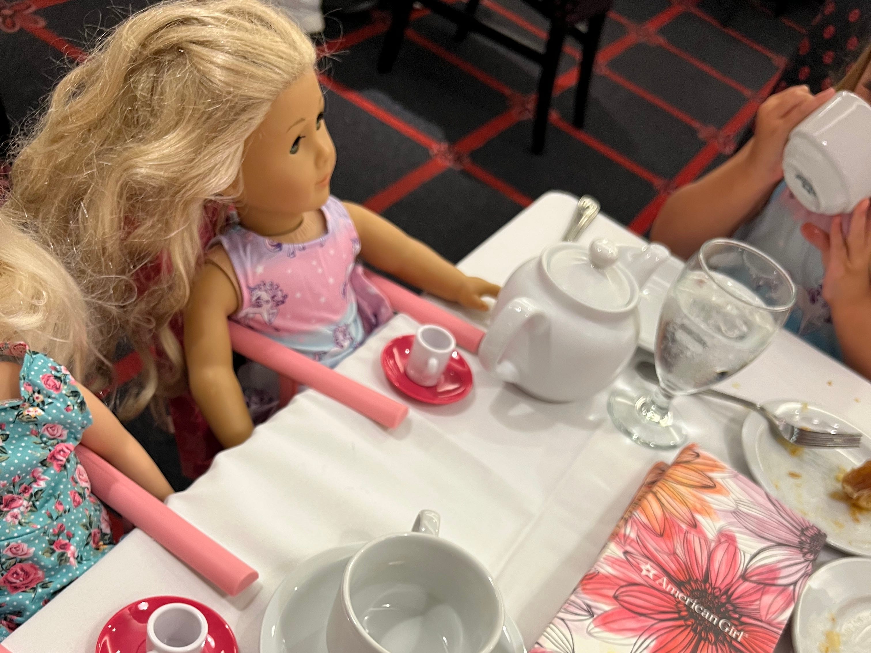 Mädchen trinkt Tee mit American Girl-Puppen