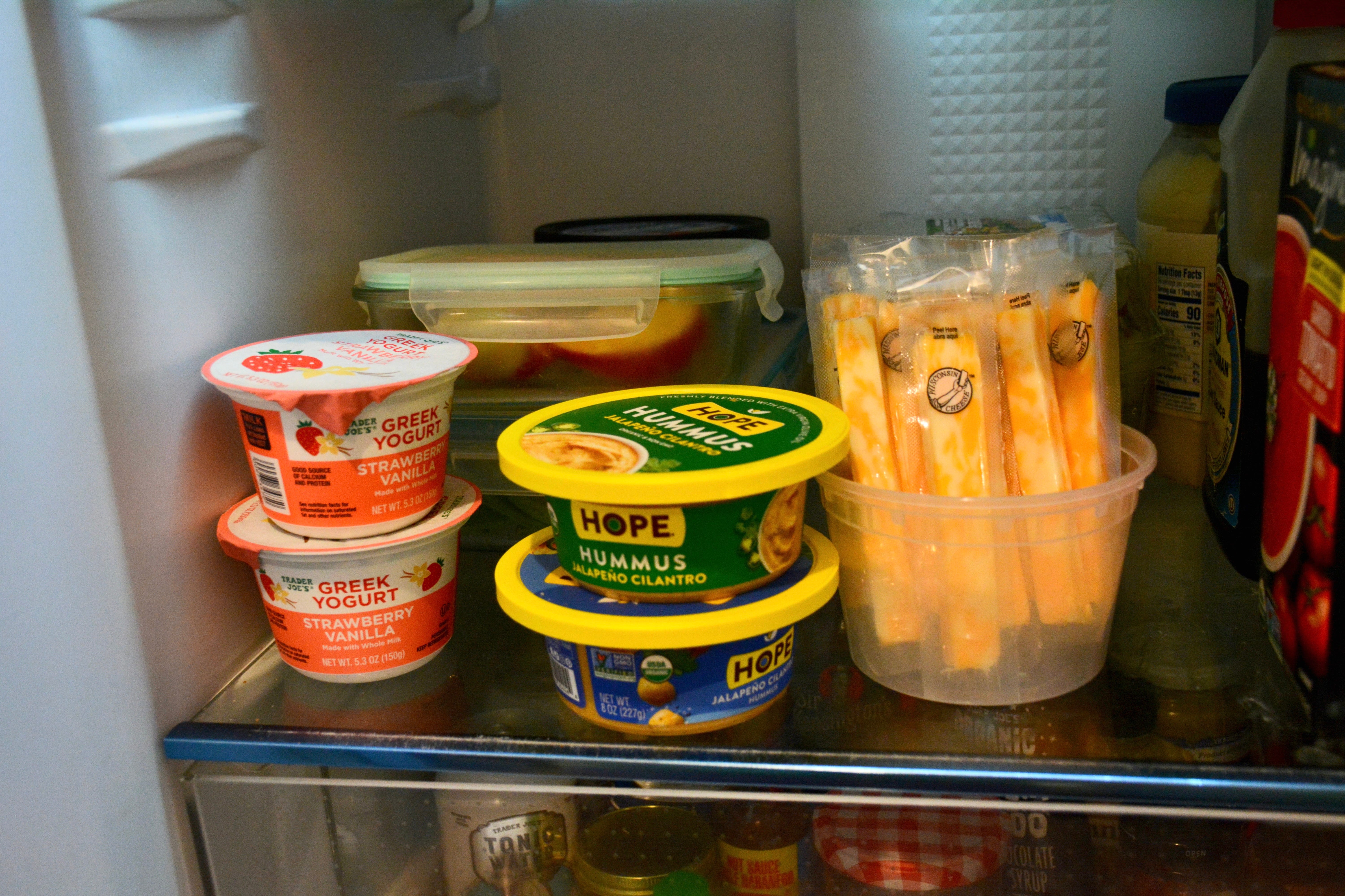 Kate Hulls „Snack-Ecke“ im Kühlschrank, komplett mit Joghurt, Hummus, Käsesticks und Tupperware gefüllt mit vorgeschnittenem Obst und Gemüse. 
