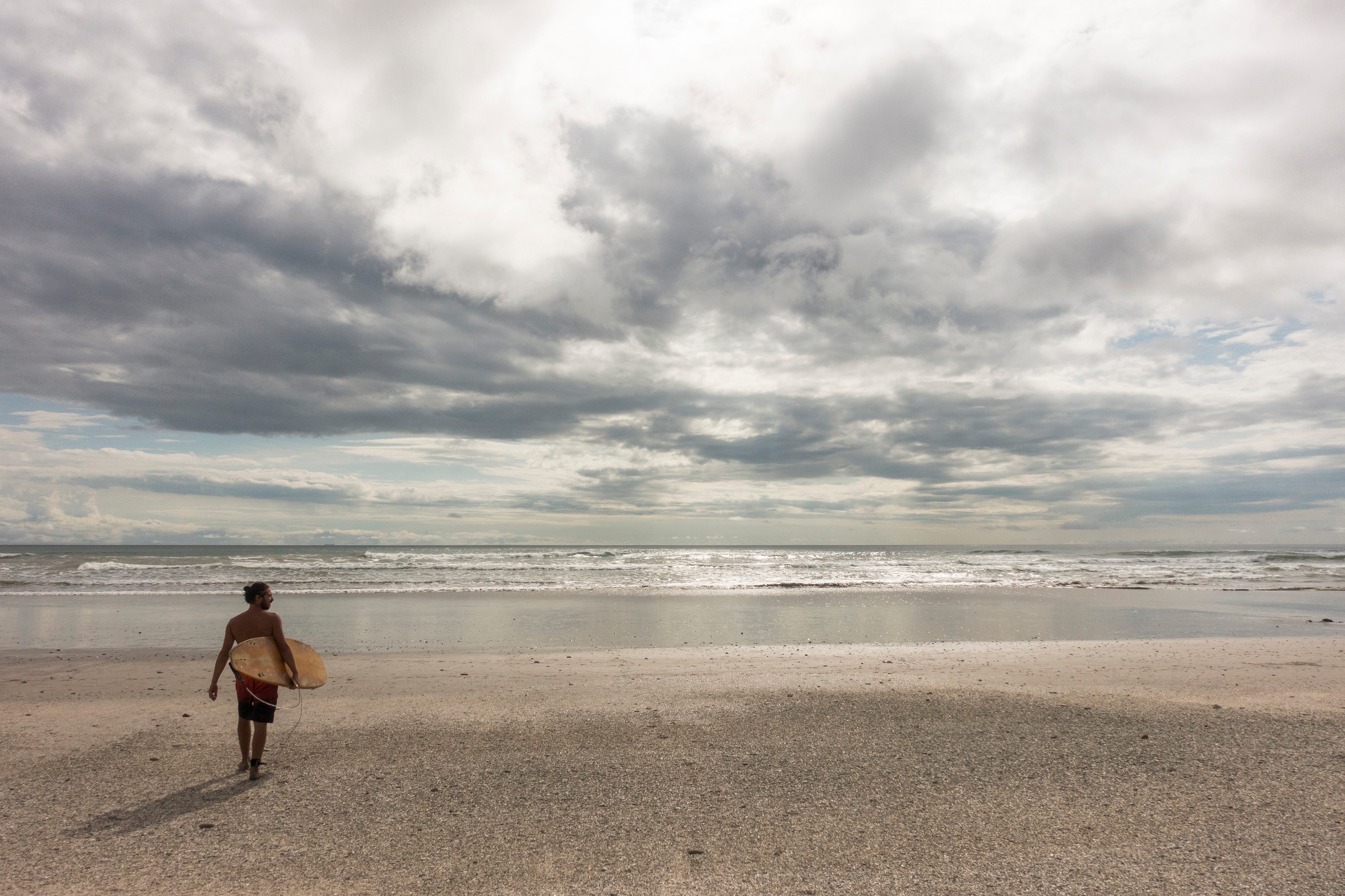 Ein Surfer steht am Strand vor dem Meer. 