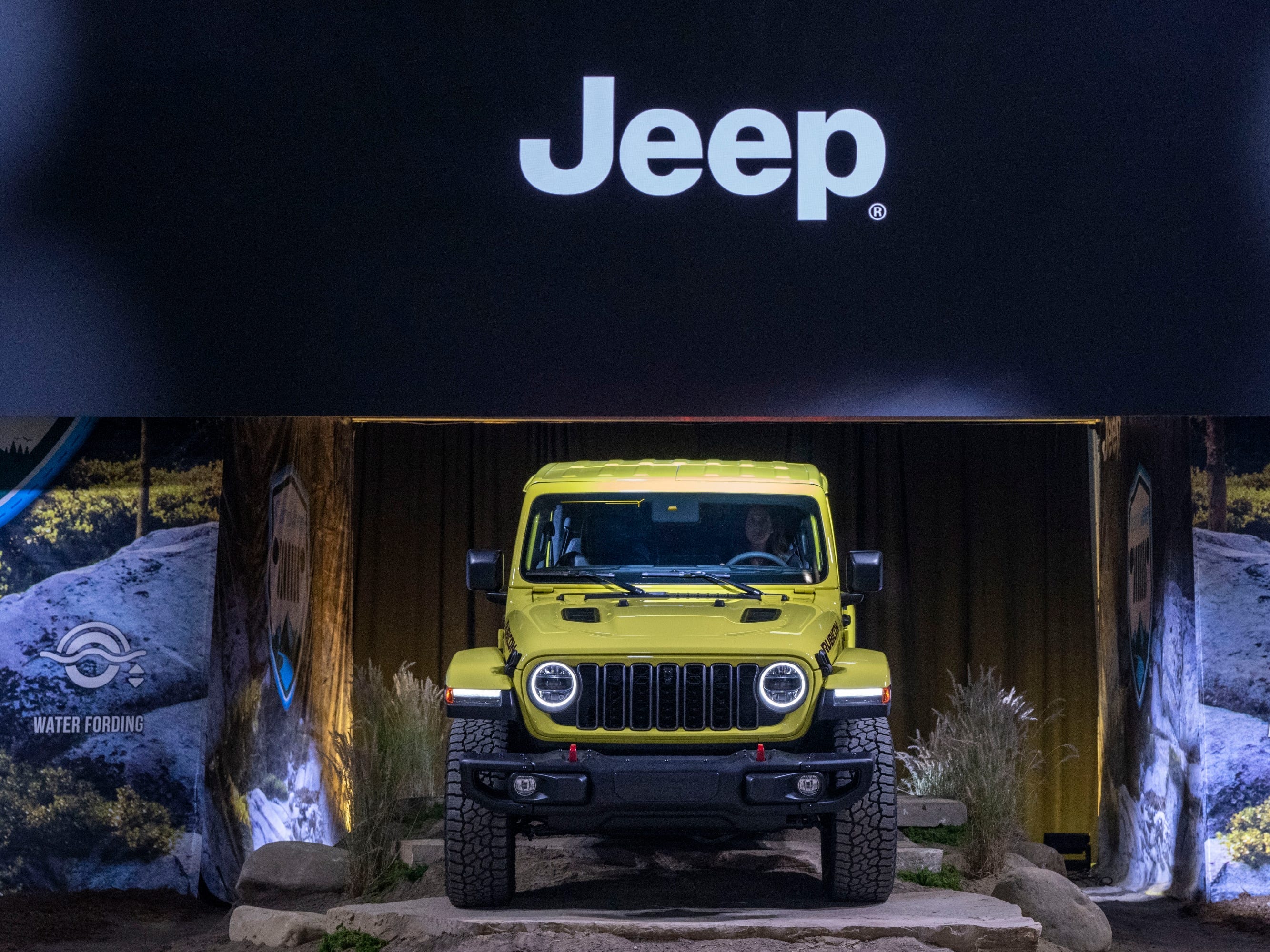 Unter einem großen schwarzen Jeep-Schild wird ein gelber SUV enthüllt.