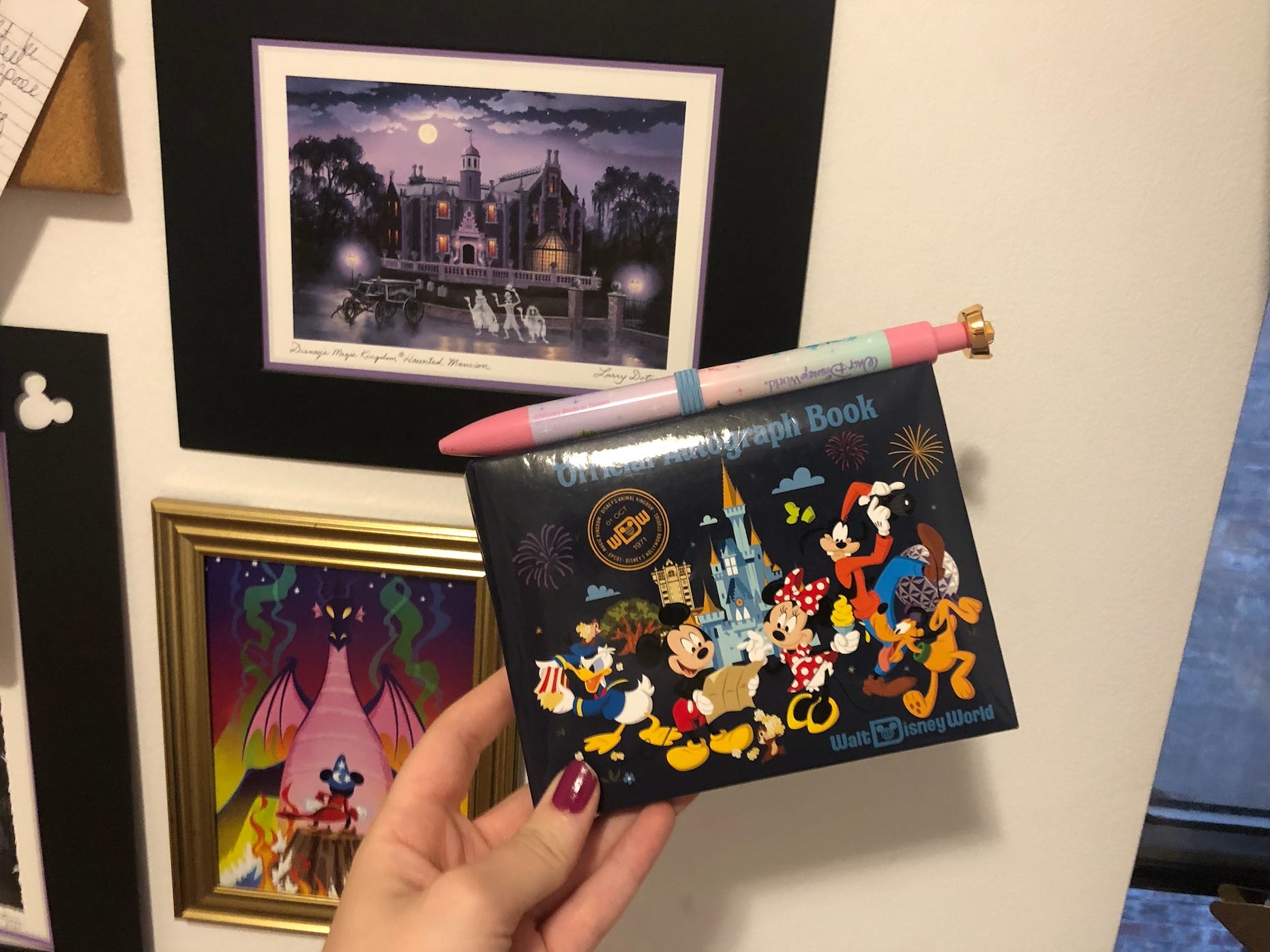 Hand hält ein offizielles Disney-Autogrammbuch mit einem originellen Stift vor Disney-Kunstwerken