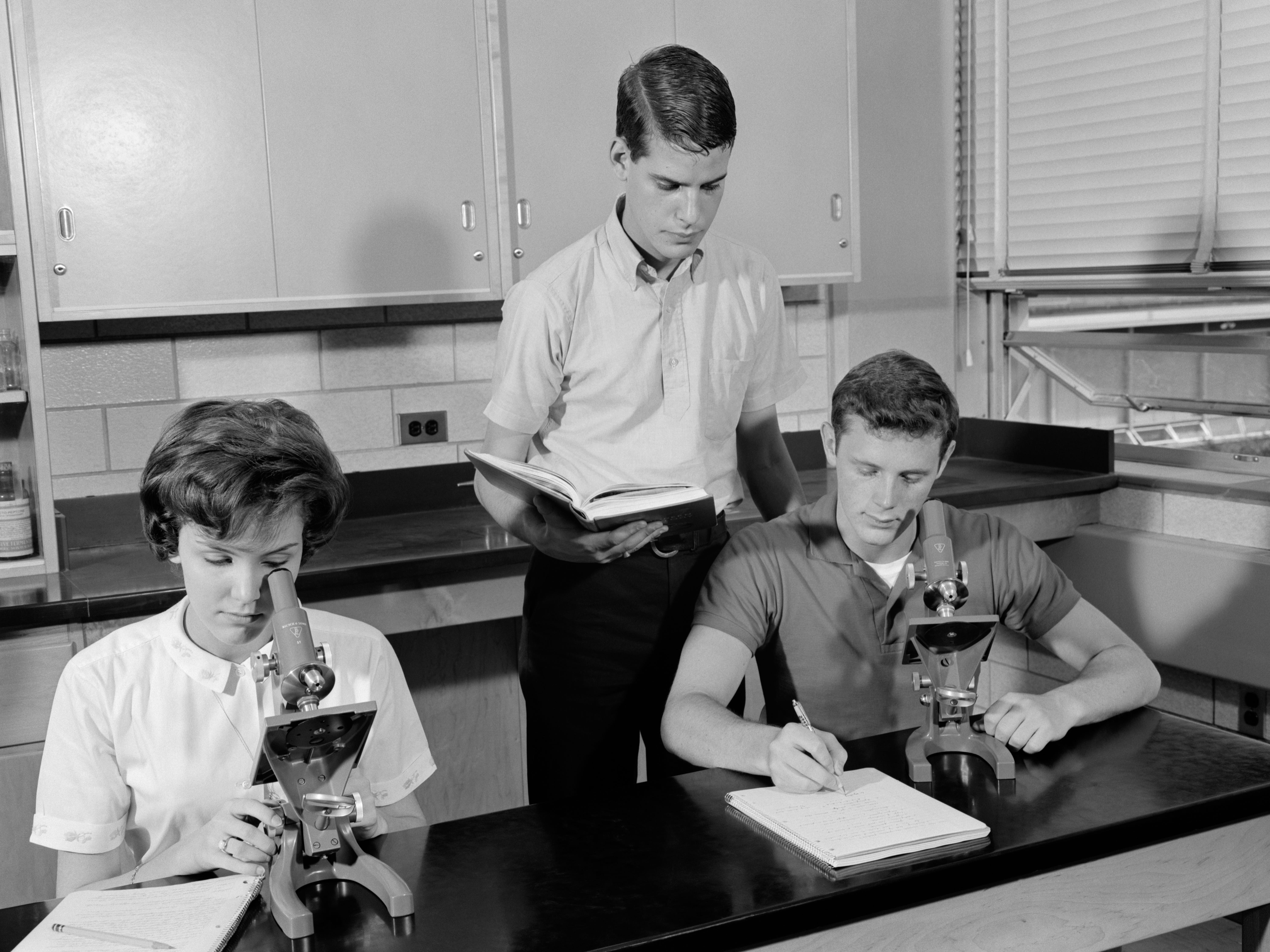Drei Oberstufenschüler im Chemieunterricht;  ein Mädchen und ein Junge, die Mikroskope benutzen.