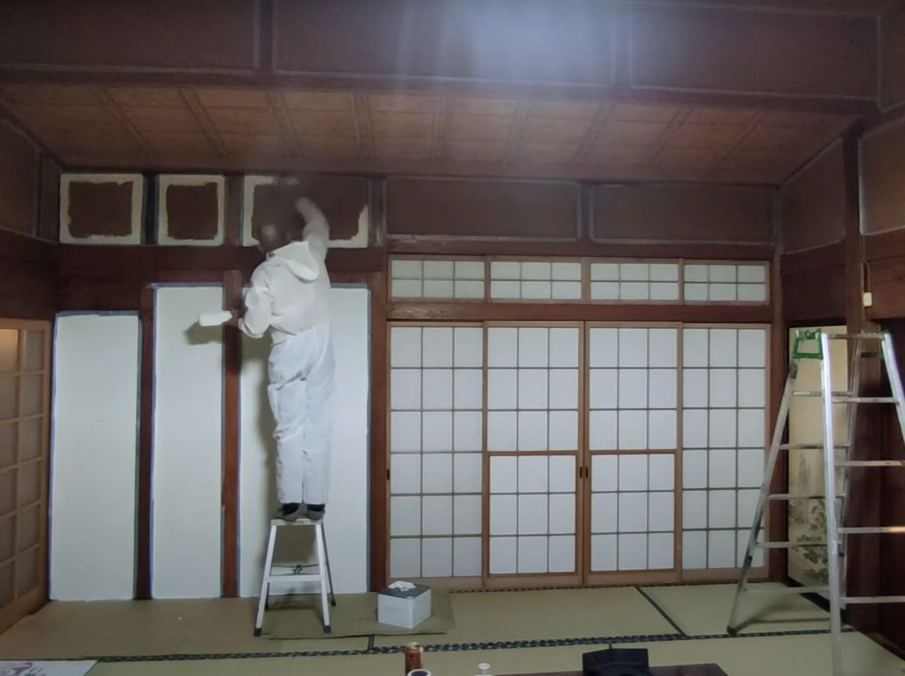 Ein Mann in einem Schutzanzug bemalt die Wände eines verlassenen Hauses auf dem japanischen Land.