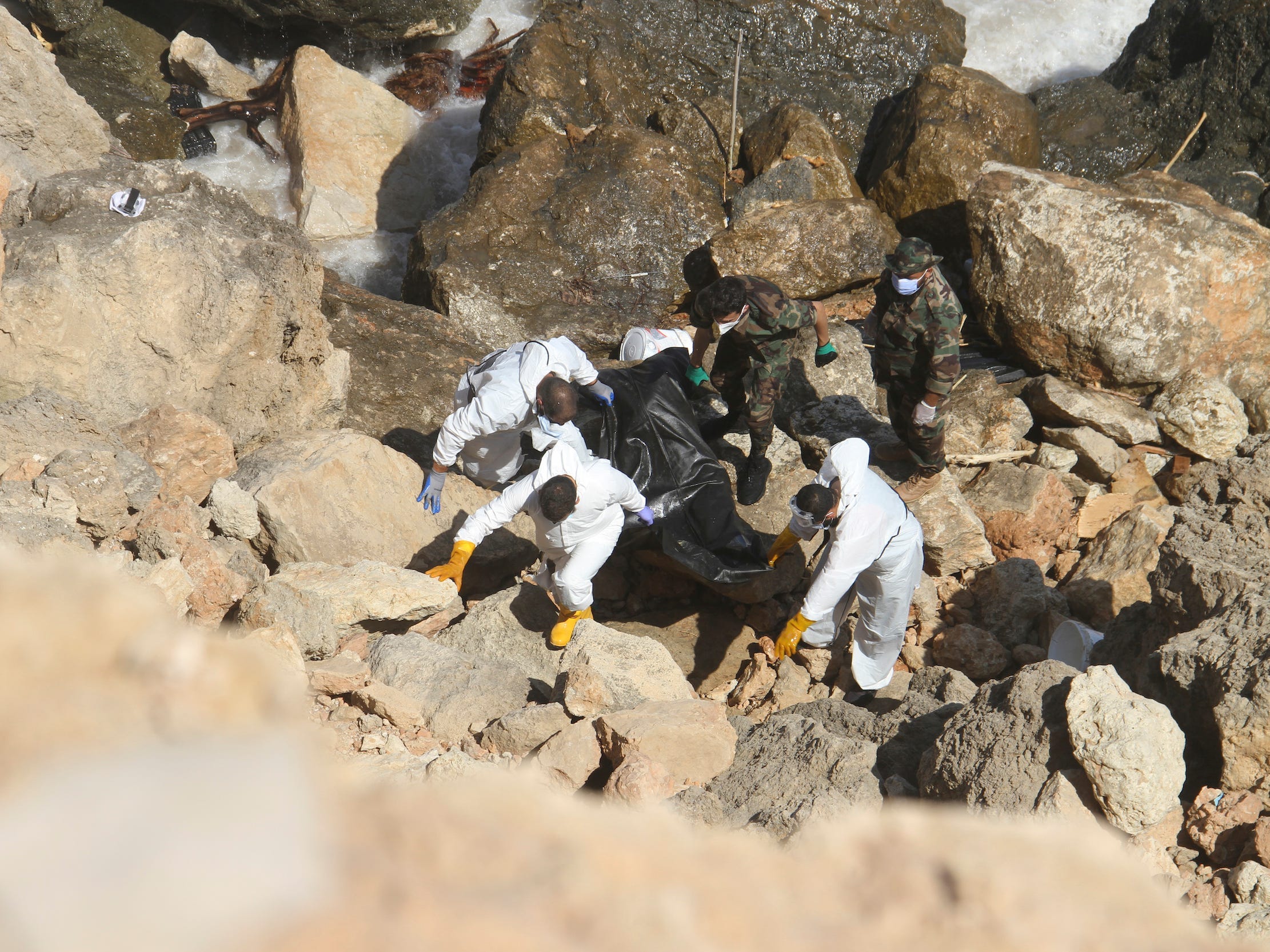 Ein Rettungsteam in weißen Anzügen trägt einen Leichensack vom felsigen Ufer von Derna hinauf.