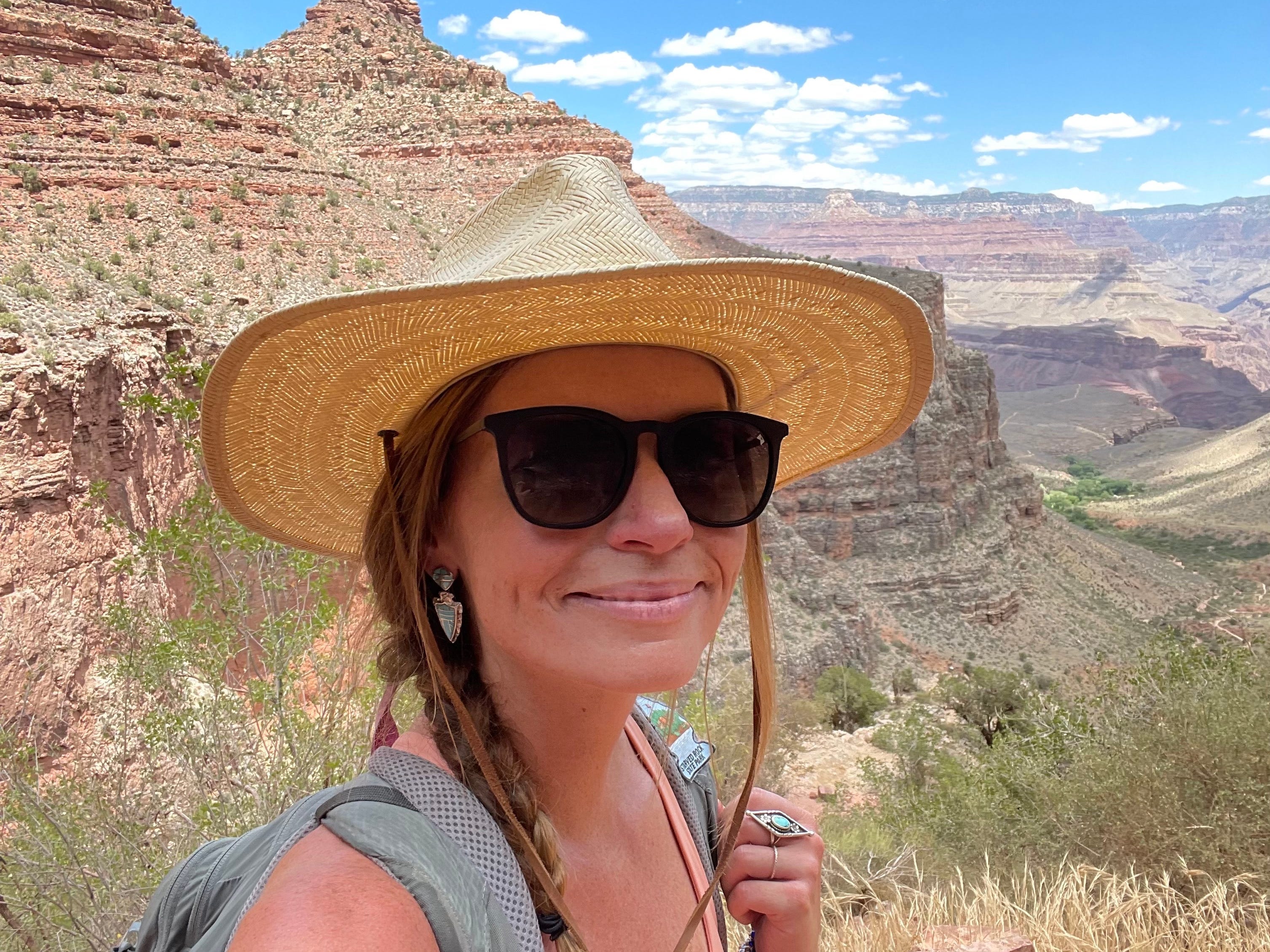 Eine Frau mit Strohhut, Rucksack und Sonnenbrille am Grand Canyon.