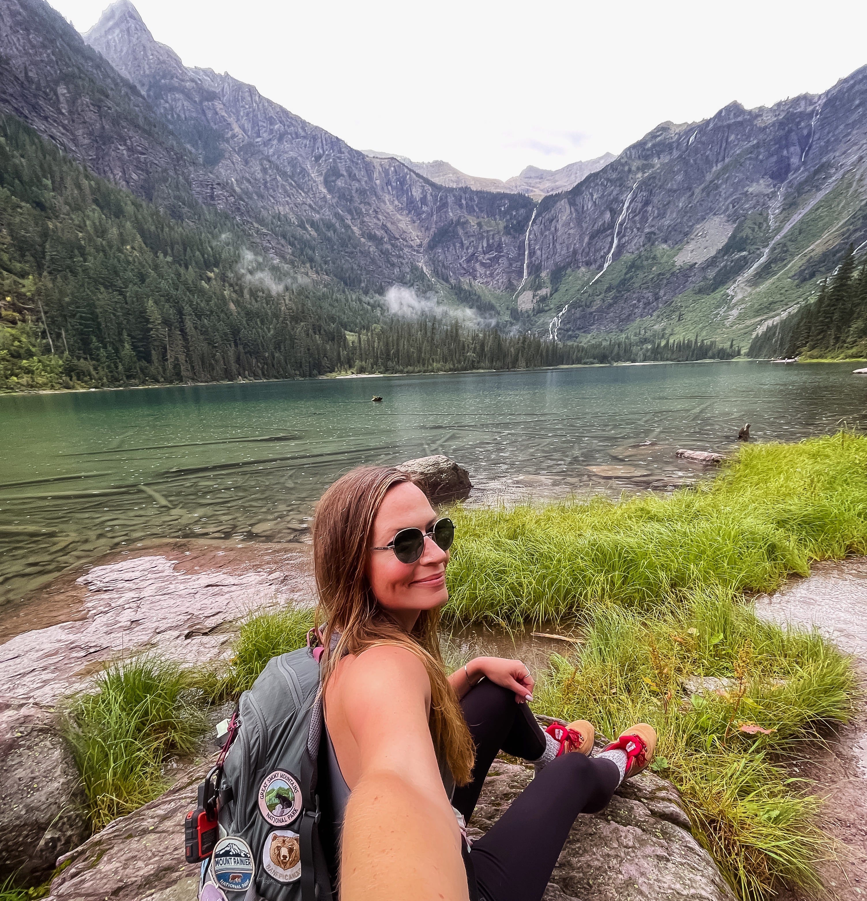 Eine Frau macht ein Selfie vor einem See und Bergen.