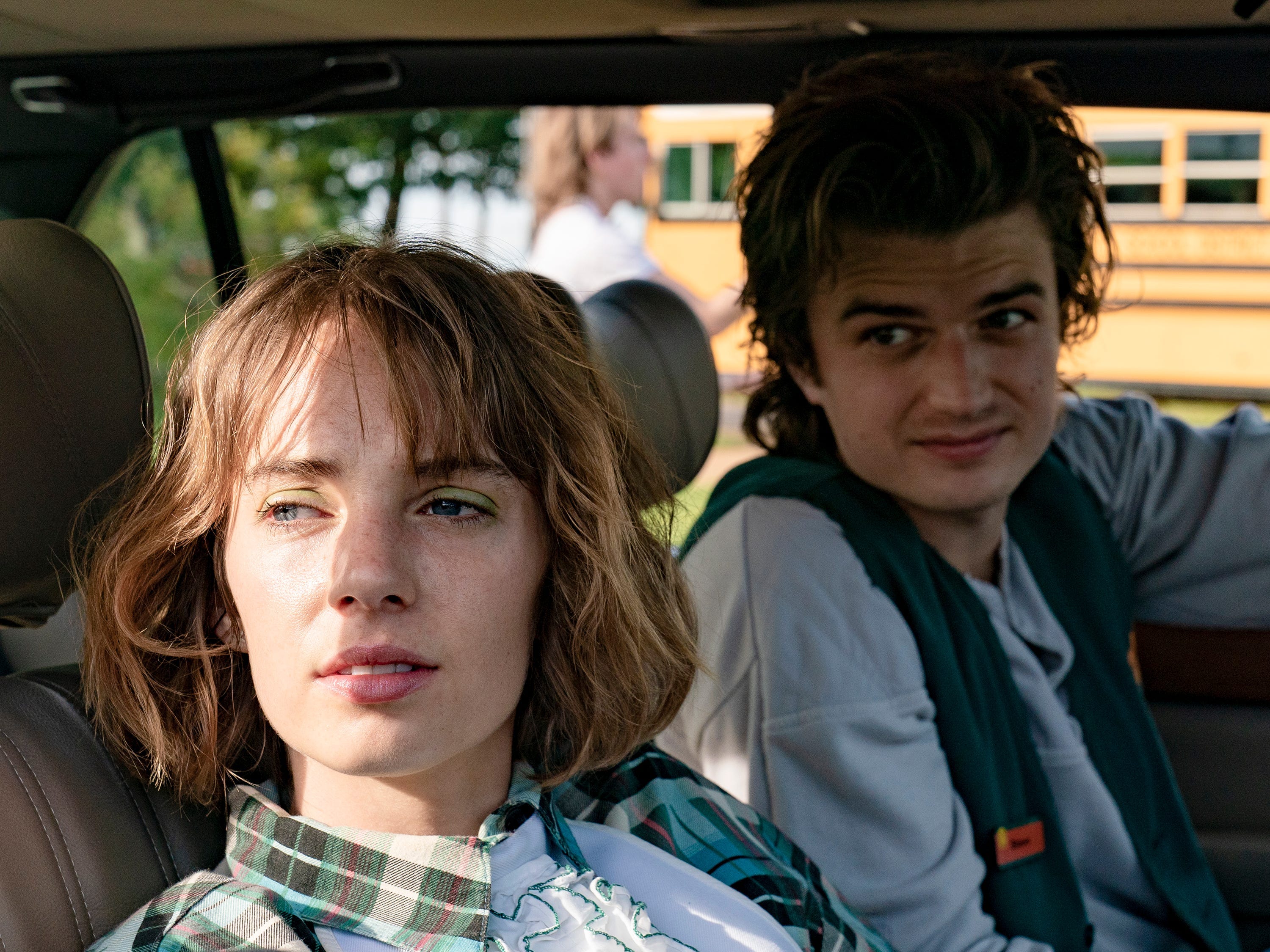 Maya Hawke und Joe Keery als Robin und Steve in Stranger Things, sitzen in einem Auto mit Steve am Steuer.  Sie schauen beide aus dem Beifahrerfenster auf etwas