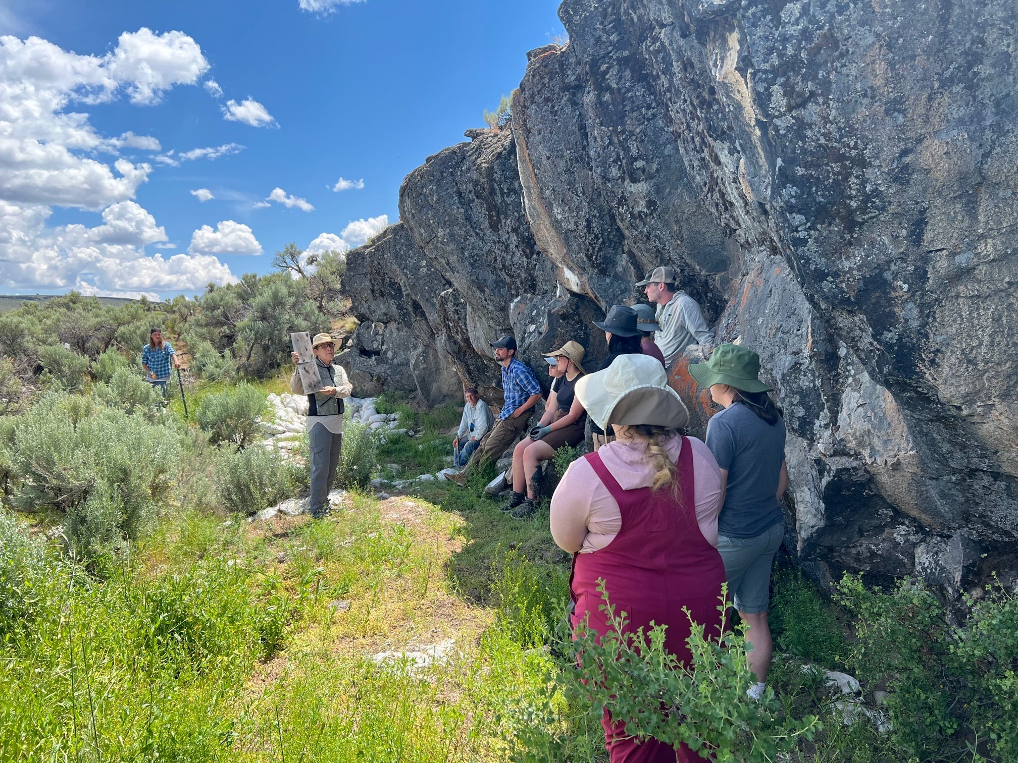 Mehrere Menschen stehen in der Nähe des Rimrock Draw Rockshelter, einer archäologischen Stätte mit über 18.000 Jahre alten Steinwerkzeugen