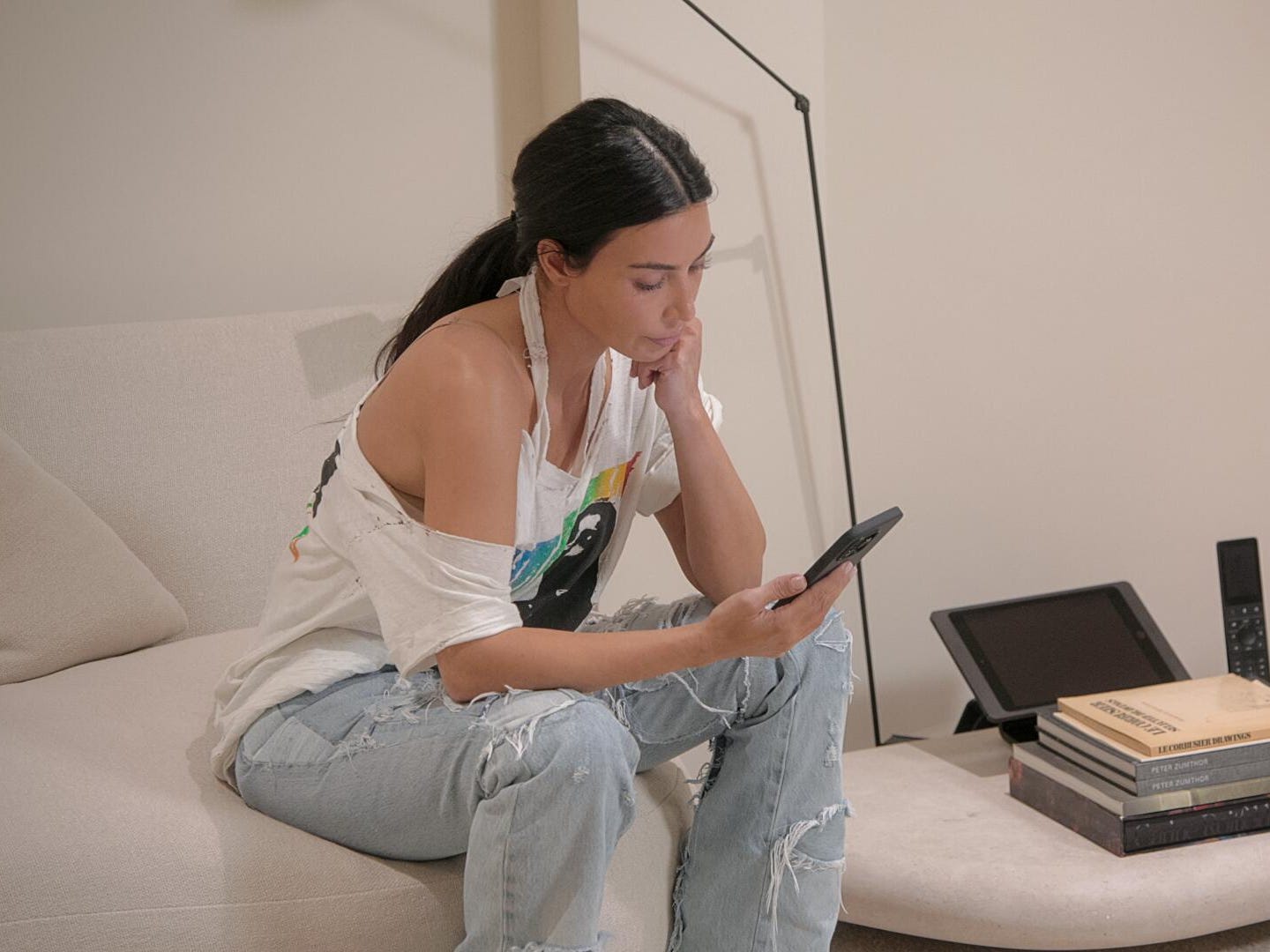 Kim Kardashian sitzt auf einer Couch und blickt besorgt auf ihr Telefon