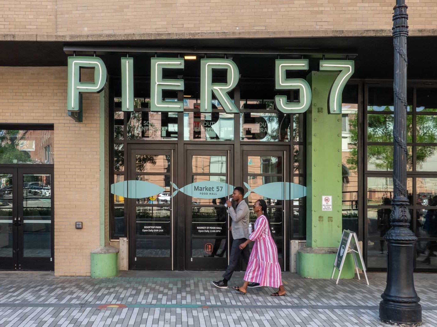 Zwei Personen gehen an einer Ladenfront mit einem Schild mit der Aufschrift „Pier 57“ vorbei