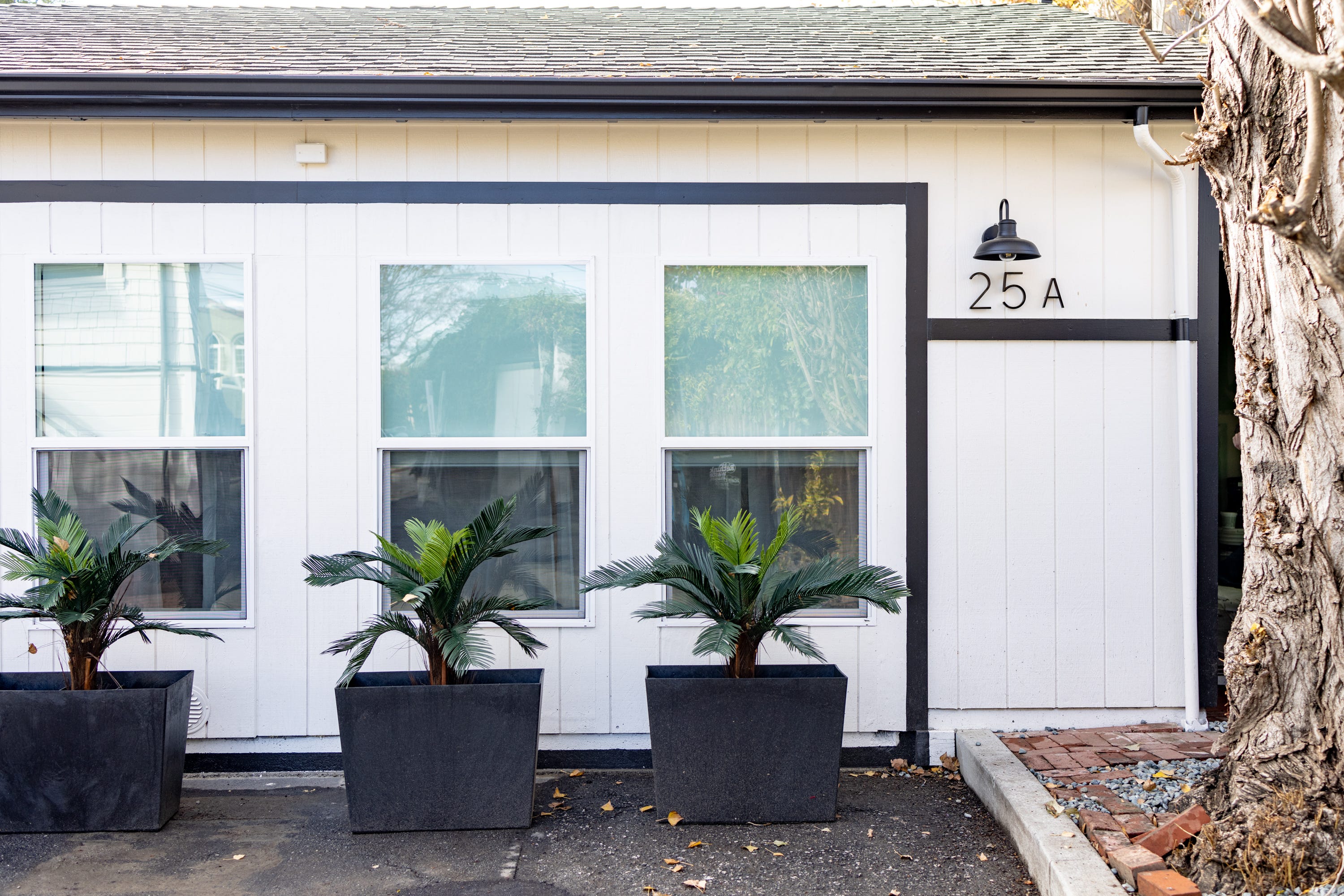 ein weißes Haus mit schwarzen Verzierungen und Pflanzen davor, eine umgebaute Garage