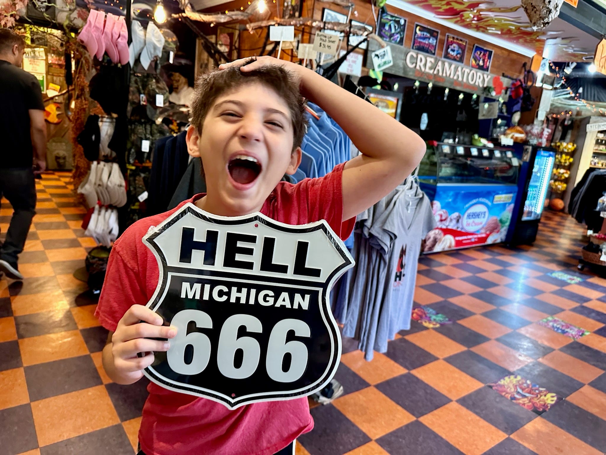 Der Sohn des Autors hält ein Straßenschild „Hell Michigan 666“ in der Hand und lacht in einem Souvenirladen 