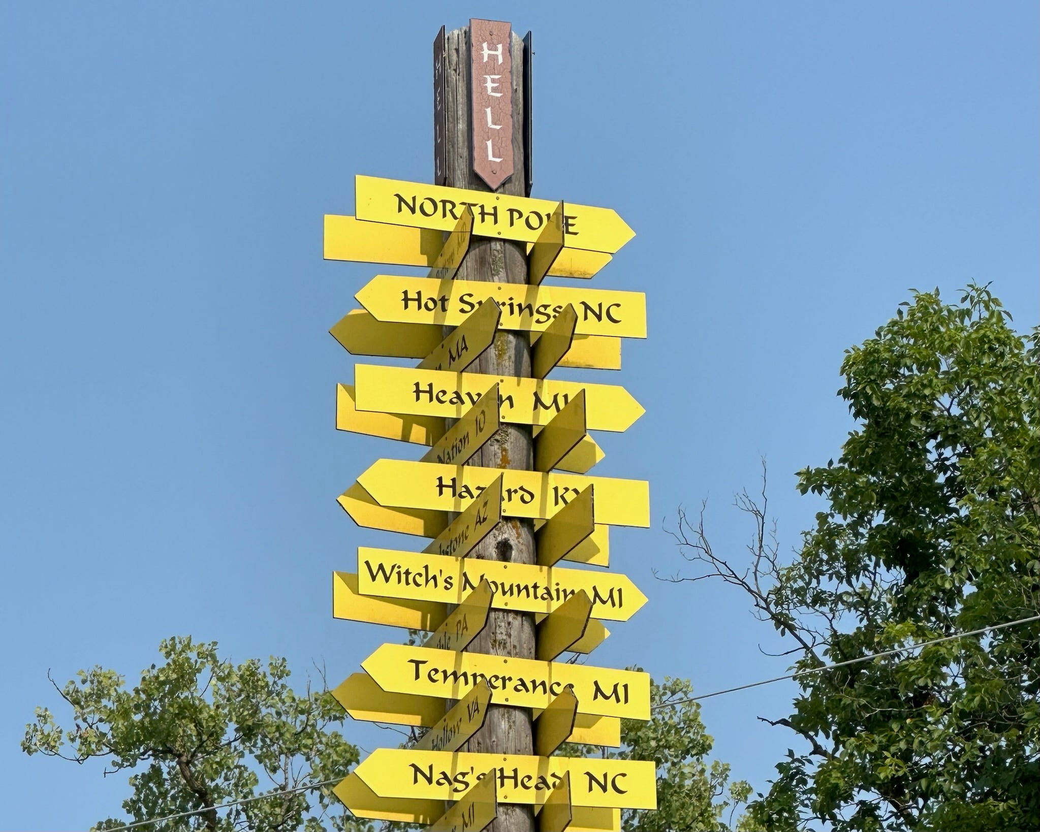 Holzpfosten bedeckt mit gelben Pfeilen mit Städtenamen, darunter Hot Springs, NC;  Himmel, MI;  und Witch's Mountain, MI 