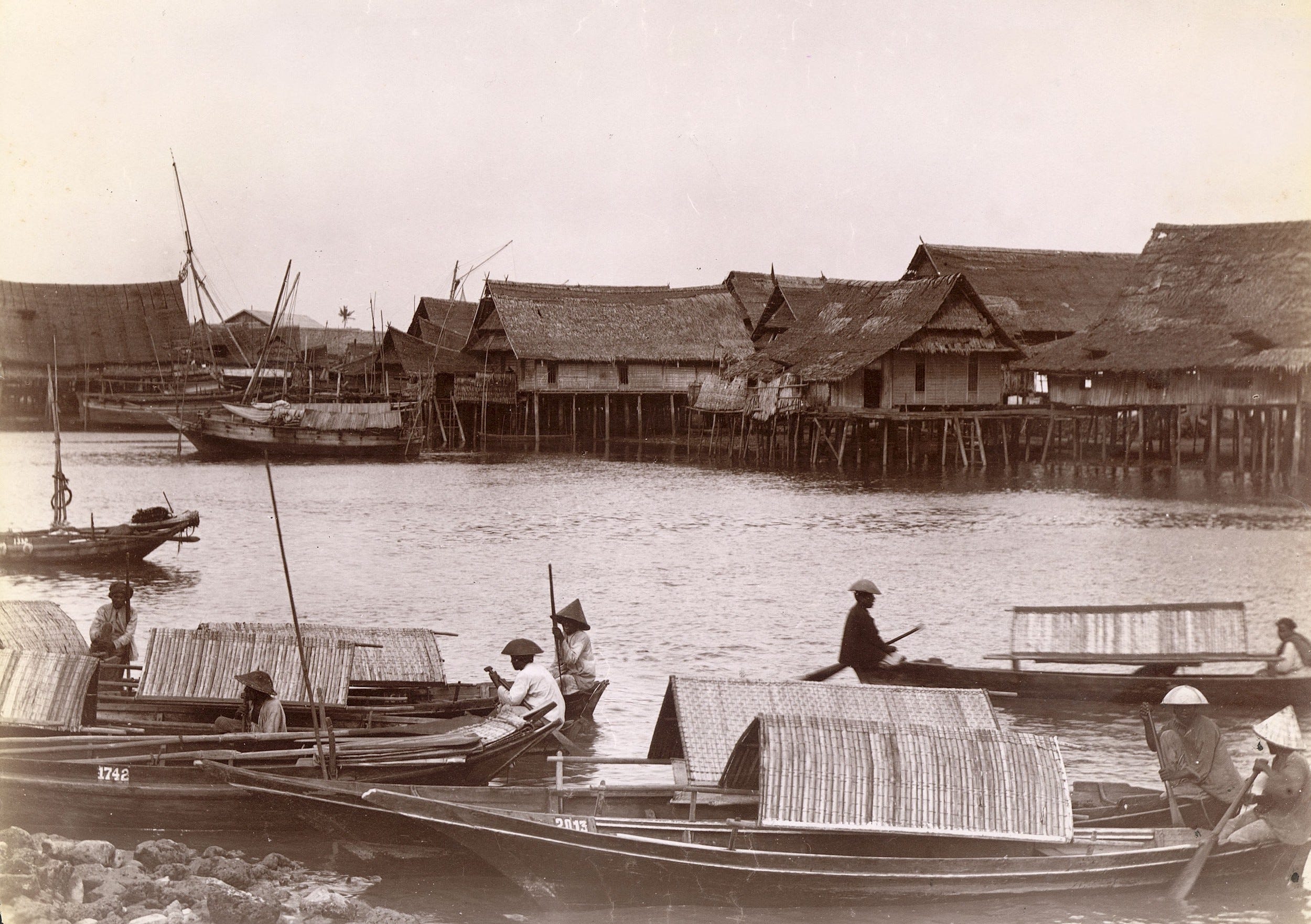 Ein Vintage-Foto von Sampan-Booten, die in der Nähe von Häusern auf Stelzen auf dem Wasser schwimmen.
