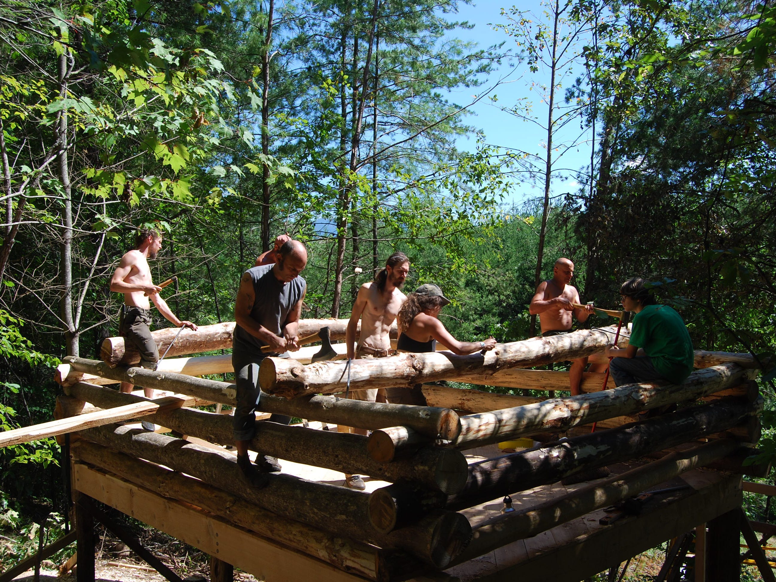 Mehrere Männer arbeiten an der Verlegung der Rundholzstämme für die Hütte.