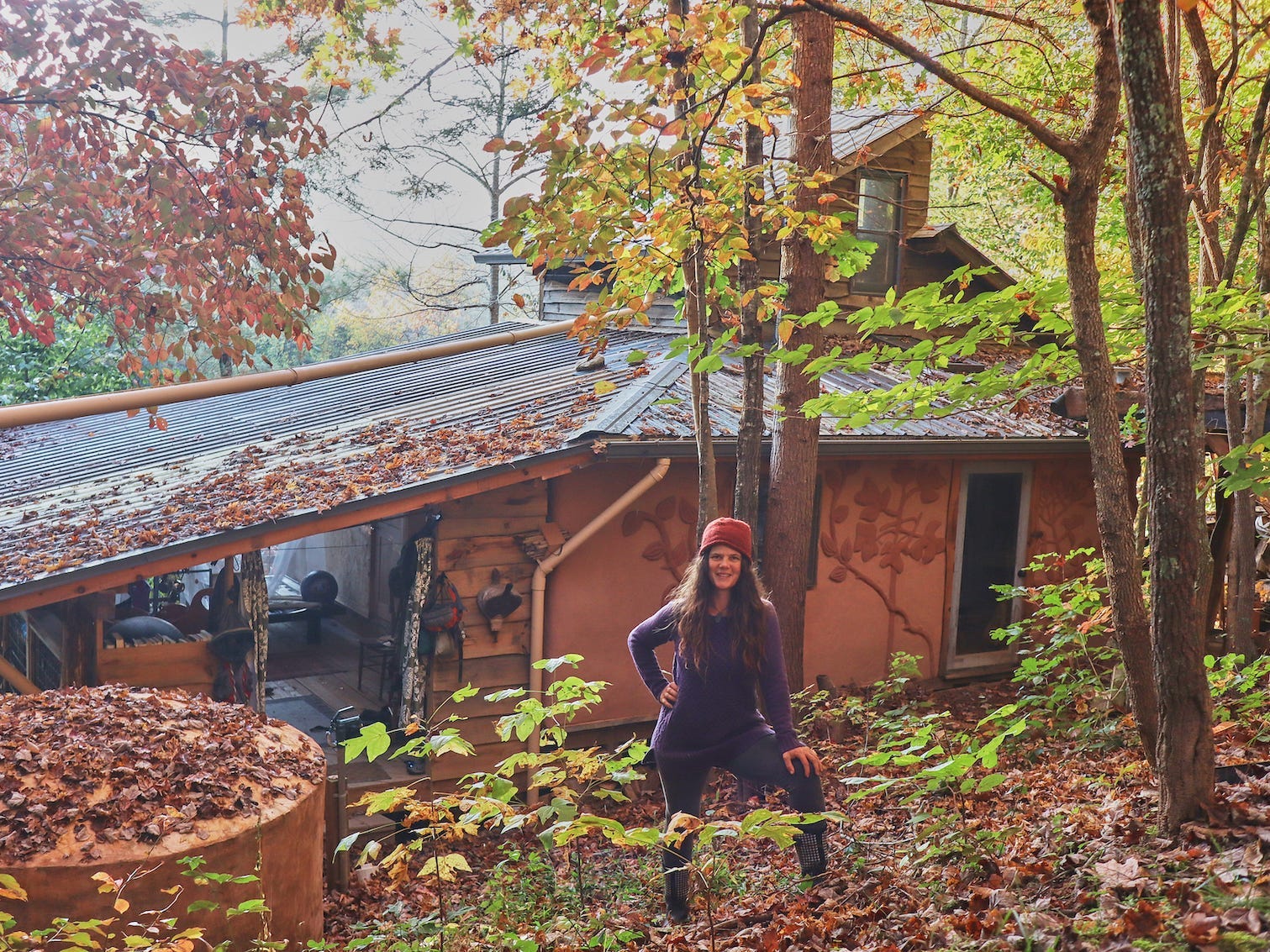 Eine Frau steht vor der Rückseite einer Blockhütte im Wald.