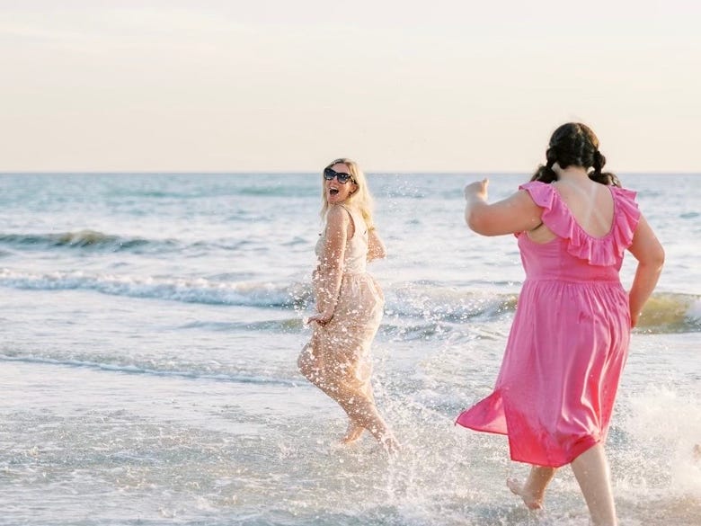 Eine blonde Frau und ein brünetter Teenager spielen am Strand in den Wellen
