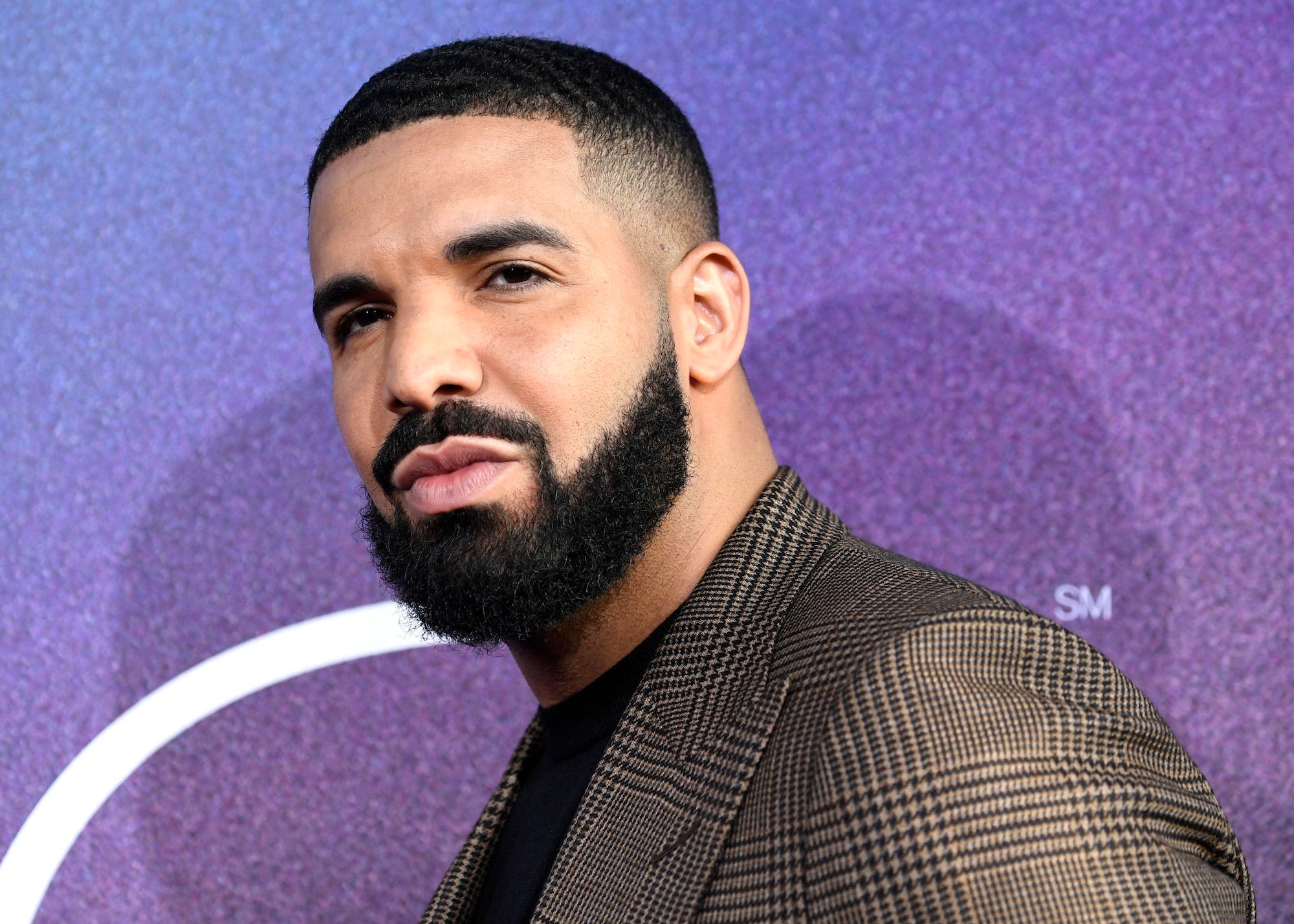 Drake in einem Anzug vor einem lila Hintergrund von den Schultern aufwärts.